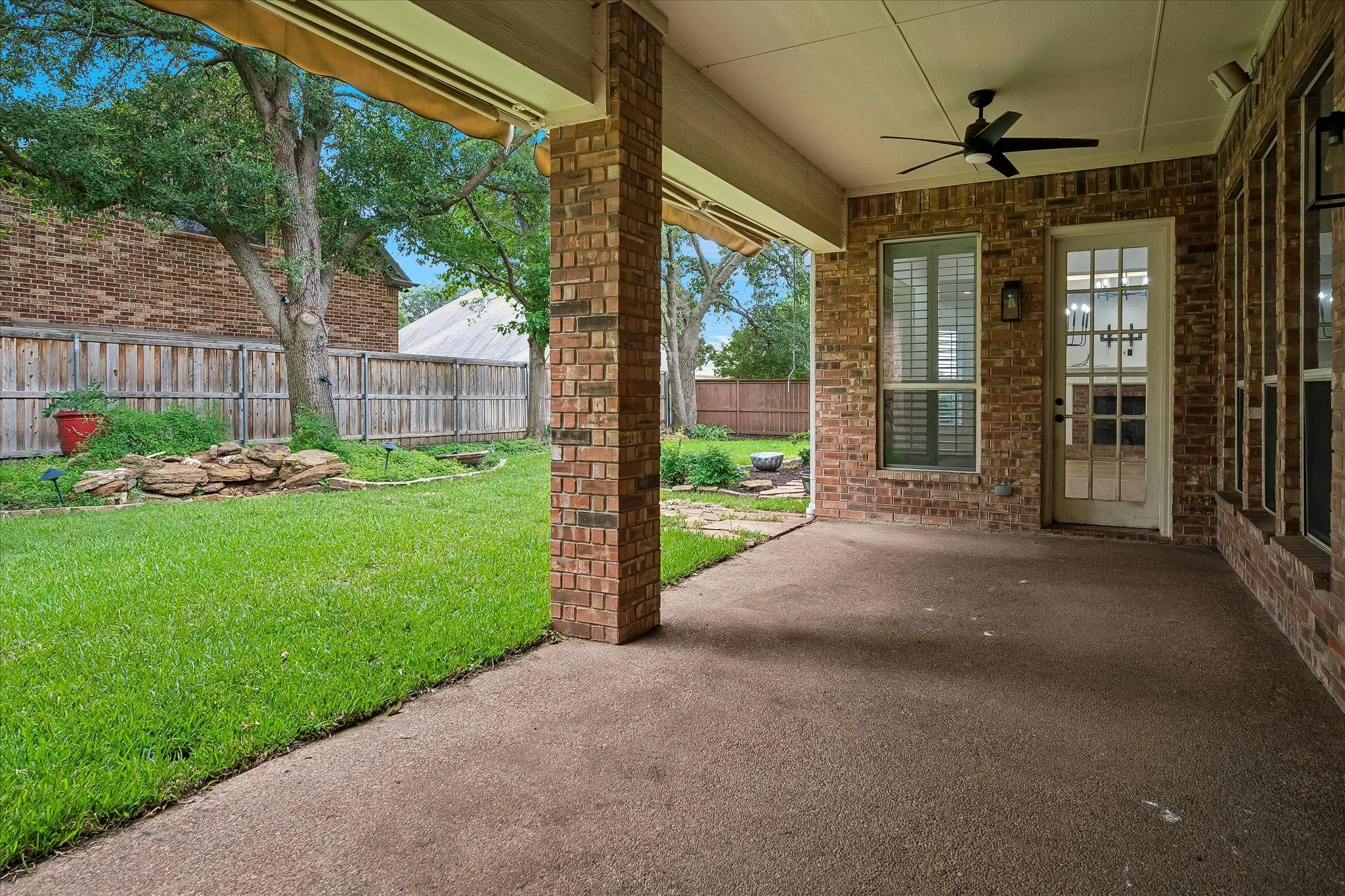 Expansive covered patio featuring a textured concrete surface, brick columns, and a ceiling fan