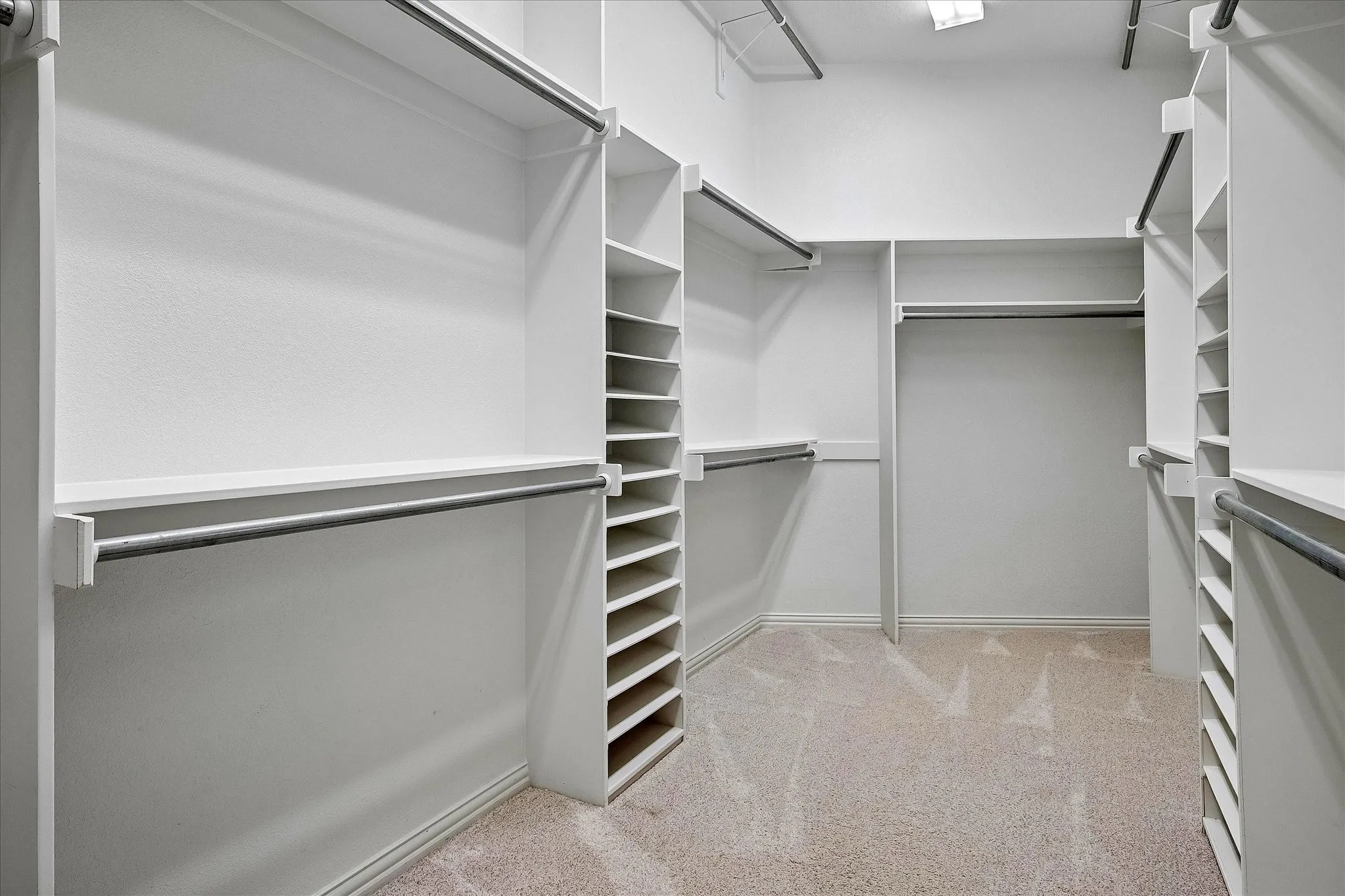 Spacious walk-in closet featuring extensive built-in shelving, multiple hanging rods, corner shelving units, and light-toned carpet flooring