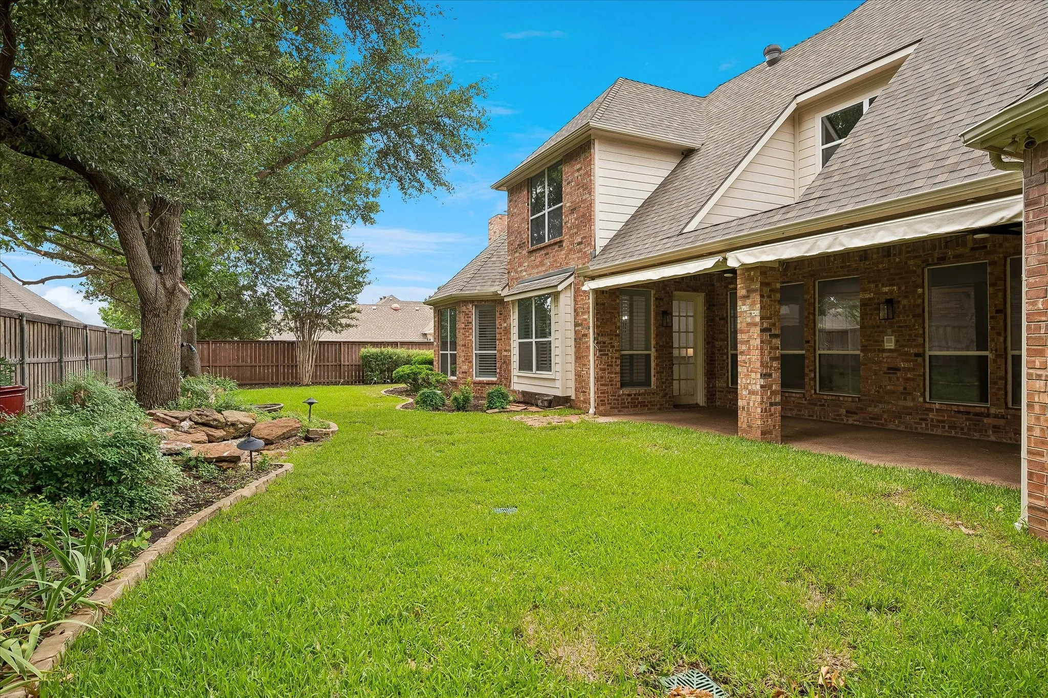 Expansive backyard featuring a manicured lawn, mature tree, and decorative rock landscaping
