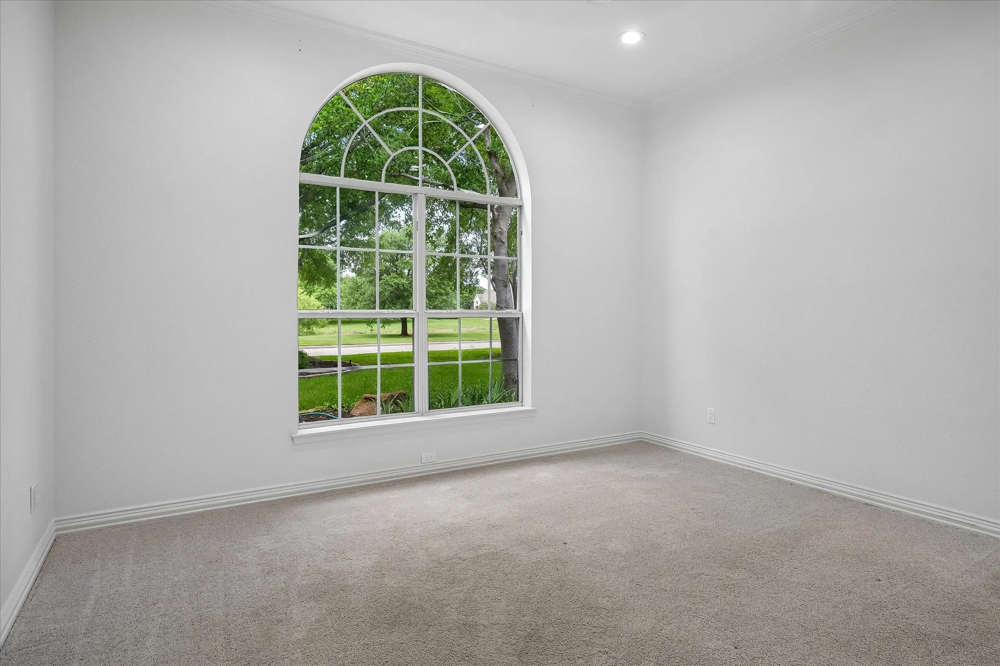 Arch-top window featuring grid patterns, soft grey carpeting, recessed lighting, white baseboards, and neutral wall tones