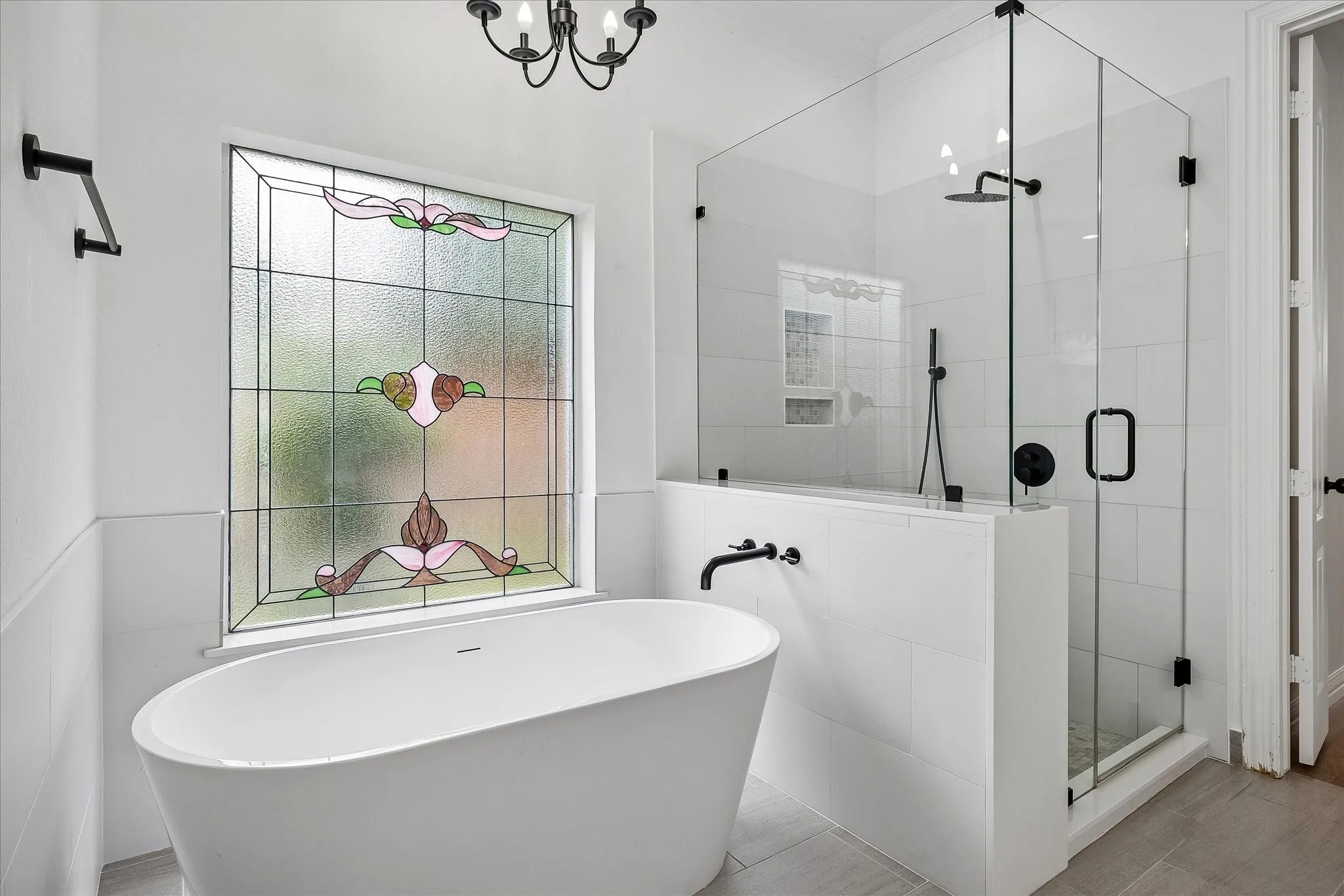 Bathroom featuring a freestanding oval tub with a wall-mounted faucet, a stained glass window, a frameless glass shower enclosure, matte black fixtures, and light-toned tile flooring