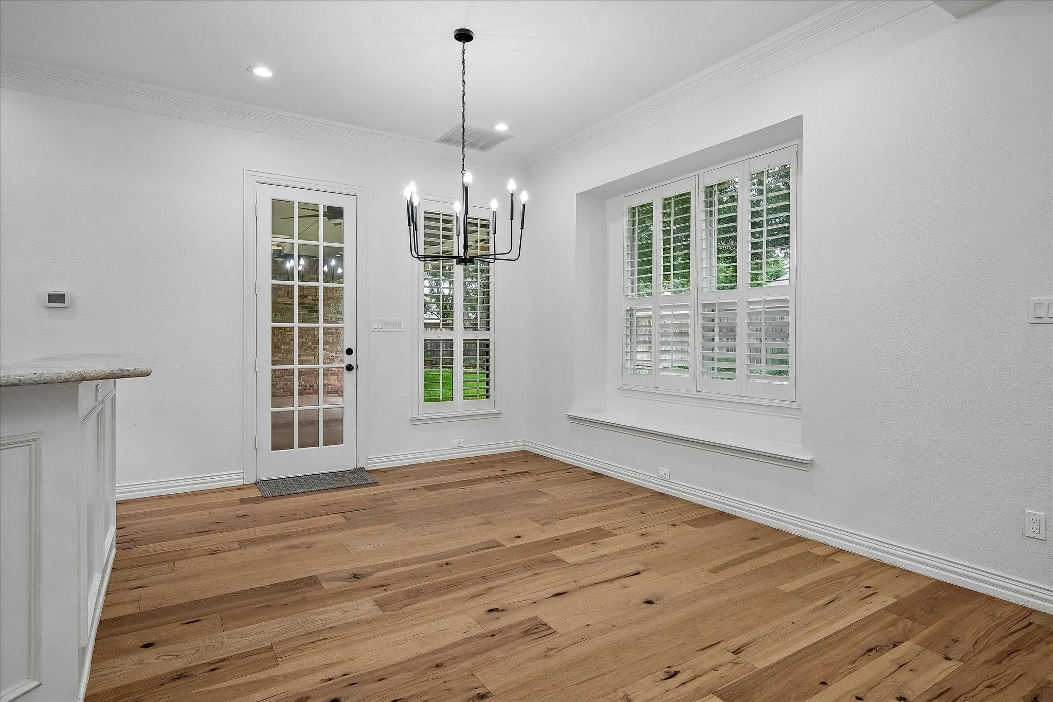 Spacious room featuring wide plank wood-finish flooring, a contemporary black chandelier, and crisp white walls