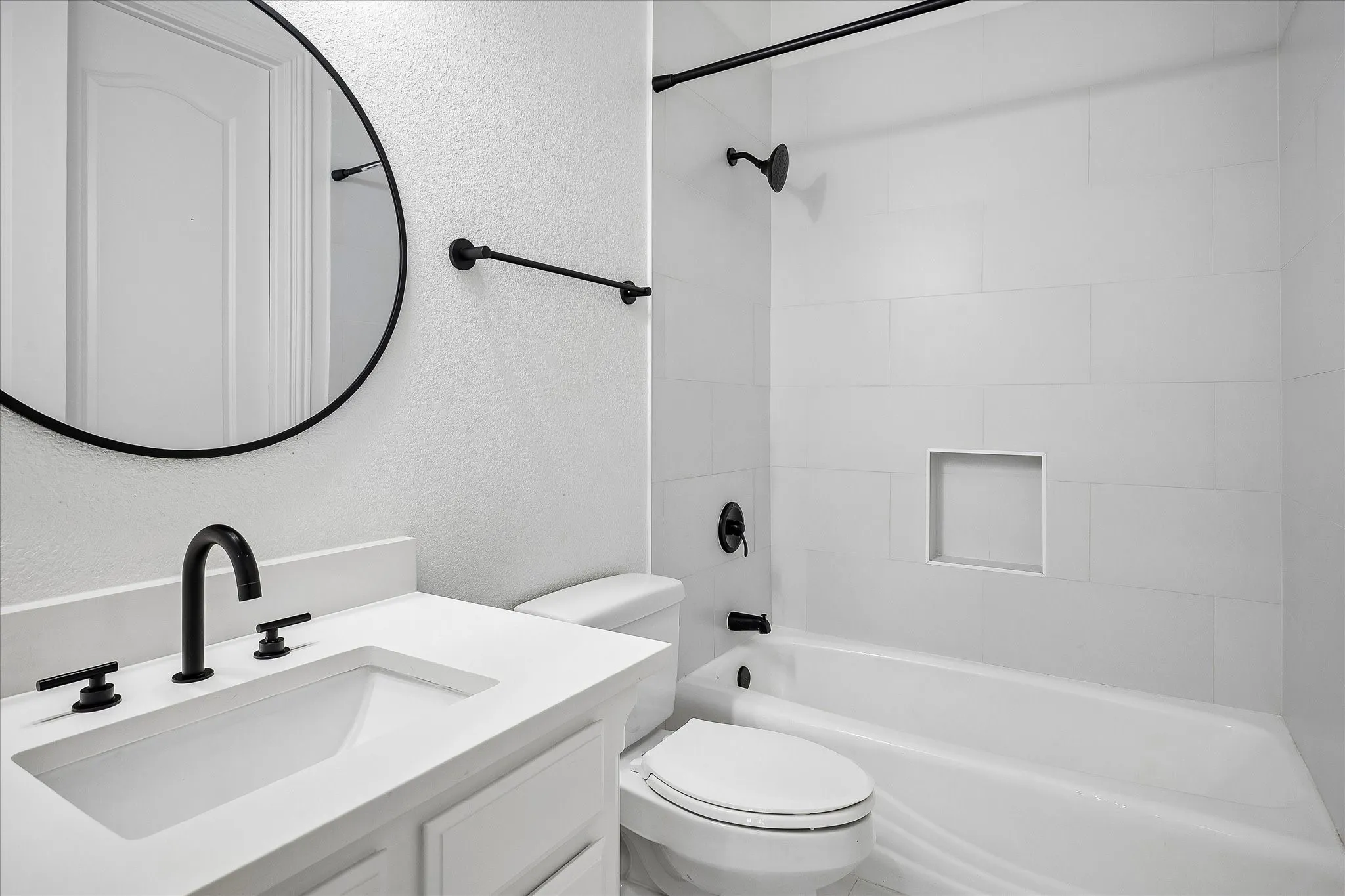 Bathroom featuring a white vanity with an integrated rectangular sink and matte black hardware, a circular framed mirror, and a white toilet