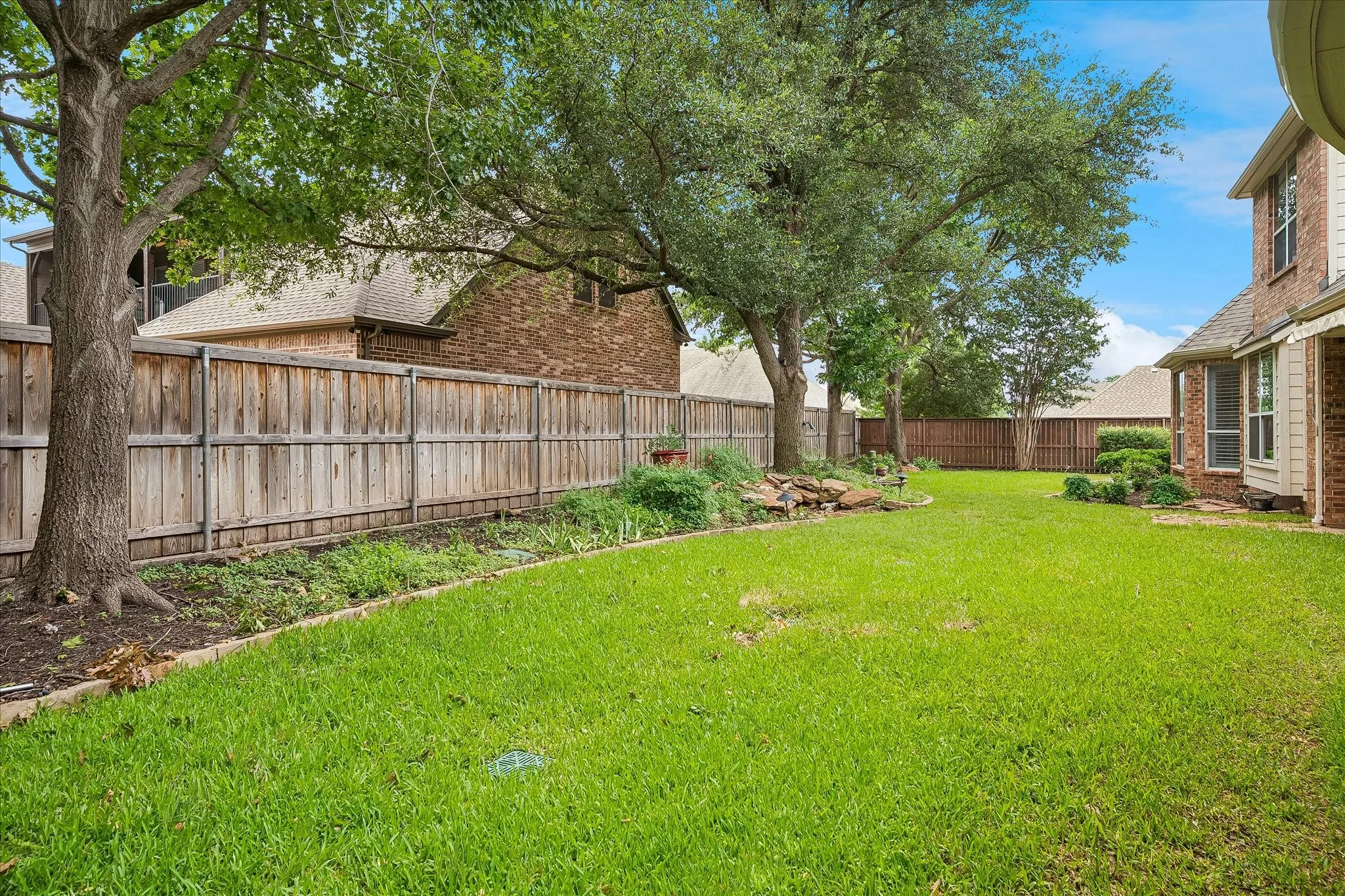 Expansive backyard featuring a lush lawn, mature shade trees, a wood privacy fence, and defined planting beds