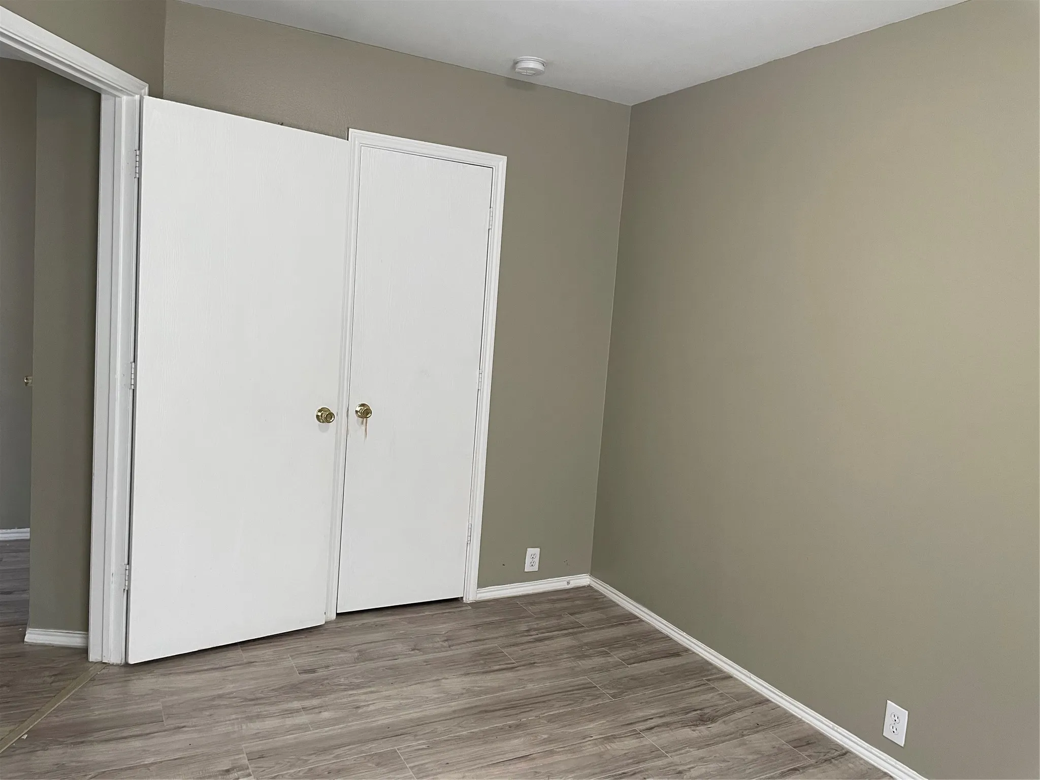 Room featuring wood-finish flooring, neutral wall paint, white baseboards, and a white bi-fold closet