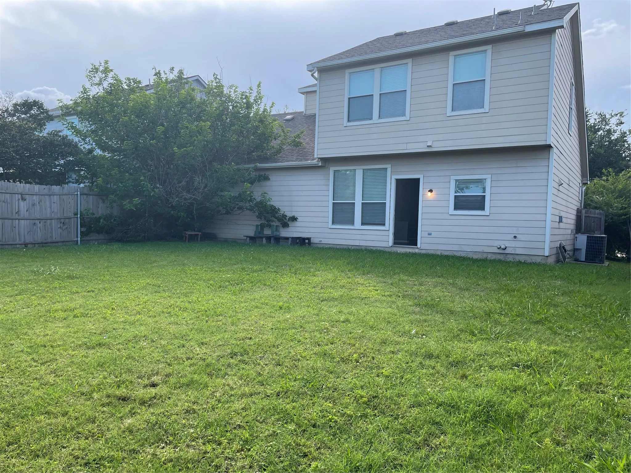 Expansive rear lawn featuring a privacy fence, established trees, and a two-story exterior with multiple windows