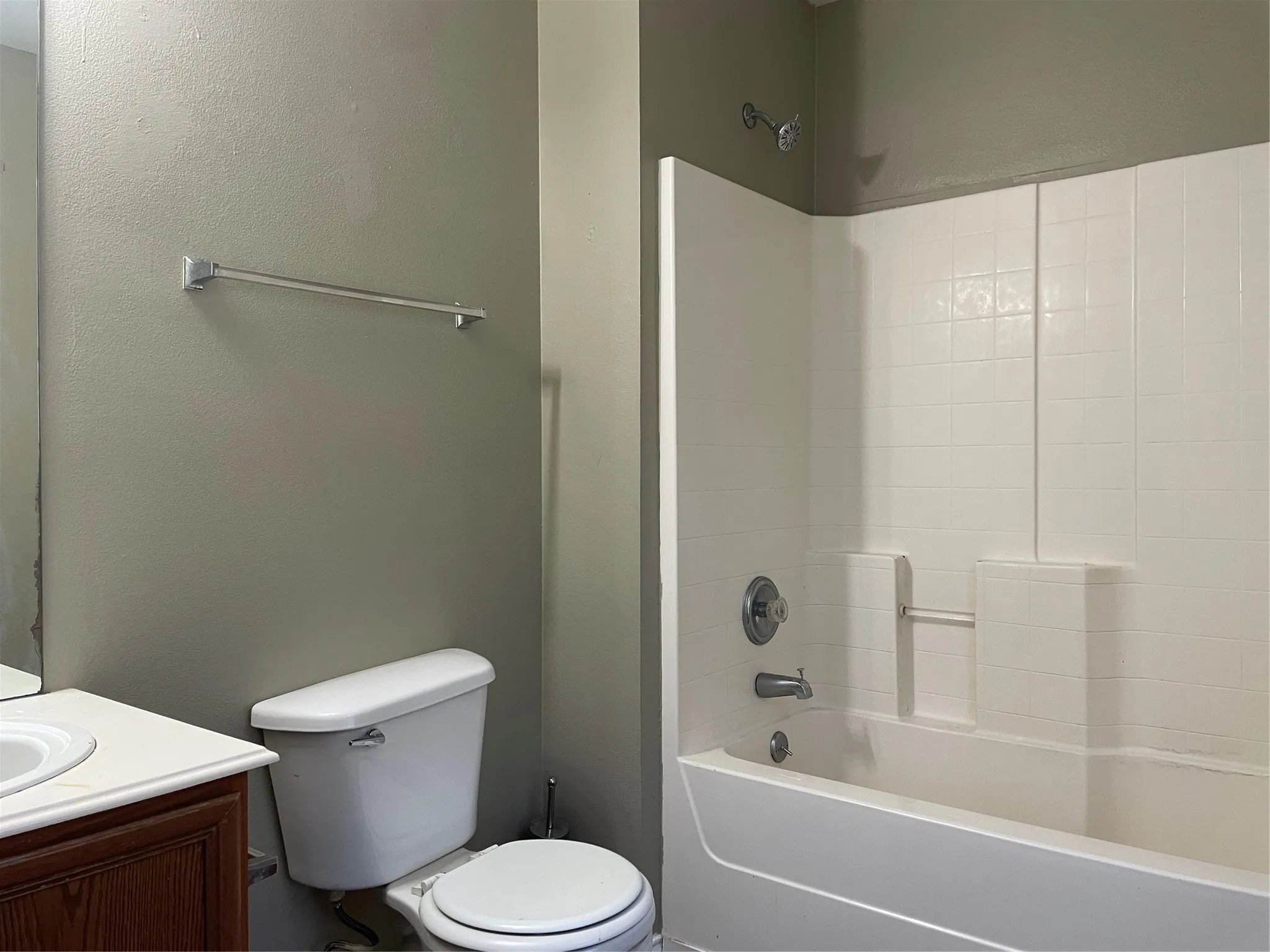 Bathroom featuring a white bathtub and shower surround, a white toilet, and a wood-finish vanity with a white countertop and integrated sink