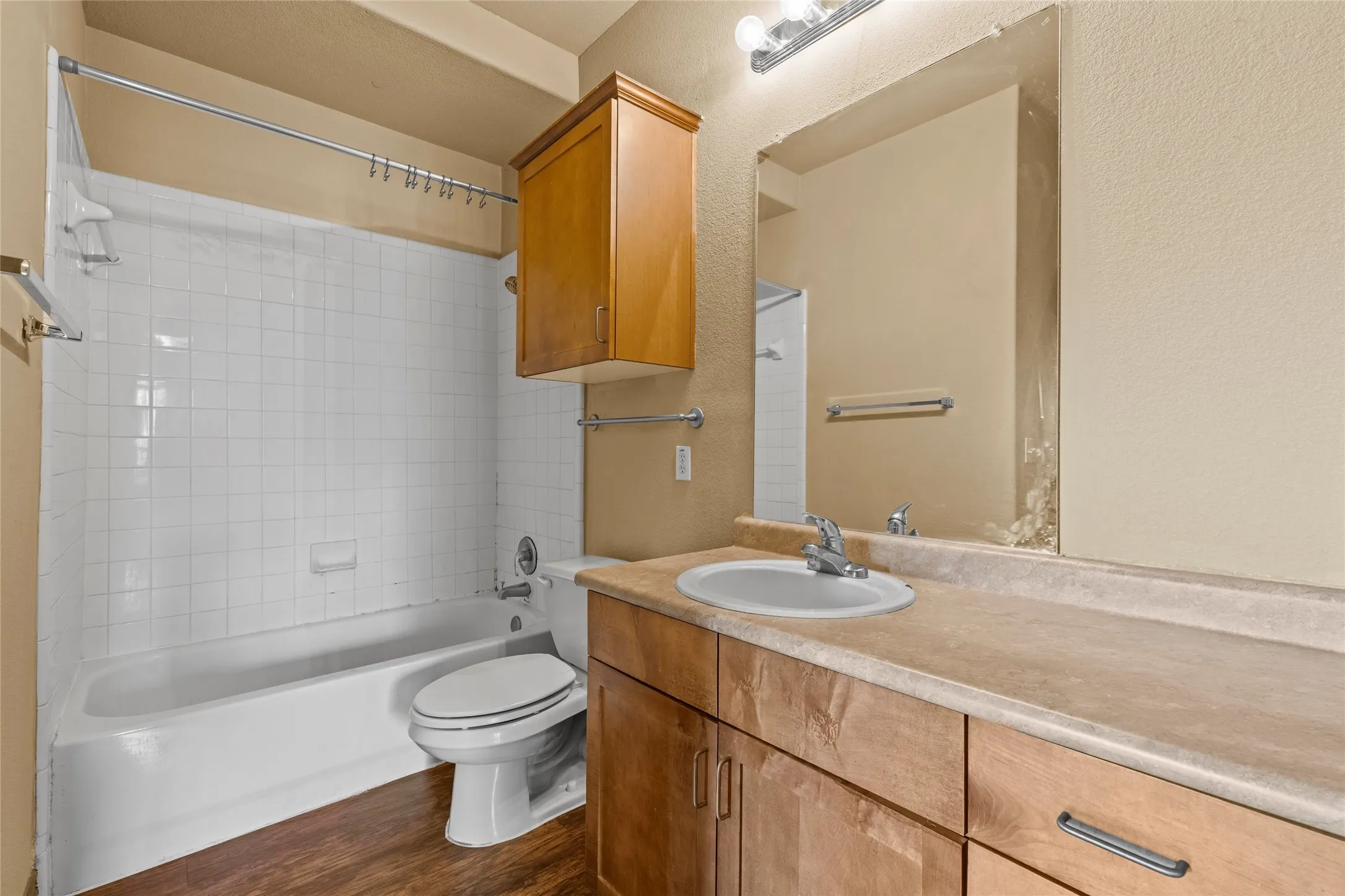 Full bathroom featuring a white tub with subway tile surround, wood-finish flooring, a light-toned vanity with an integrated sink, and an expansive wall-mounted mirror
