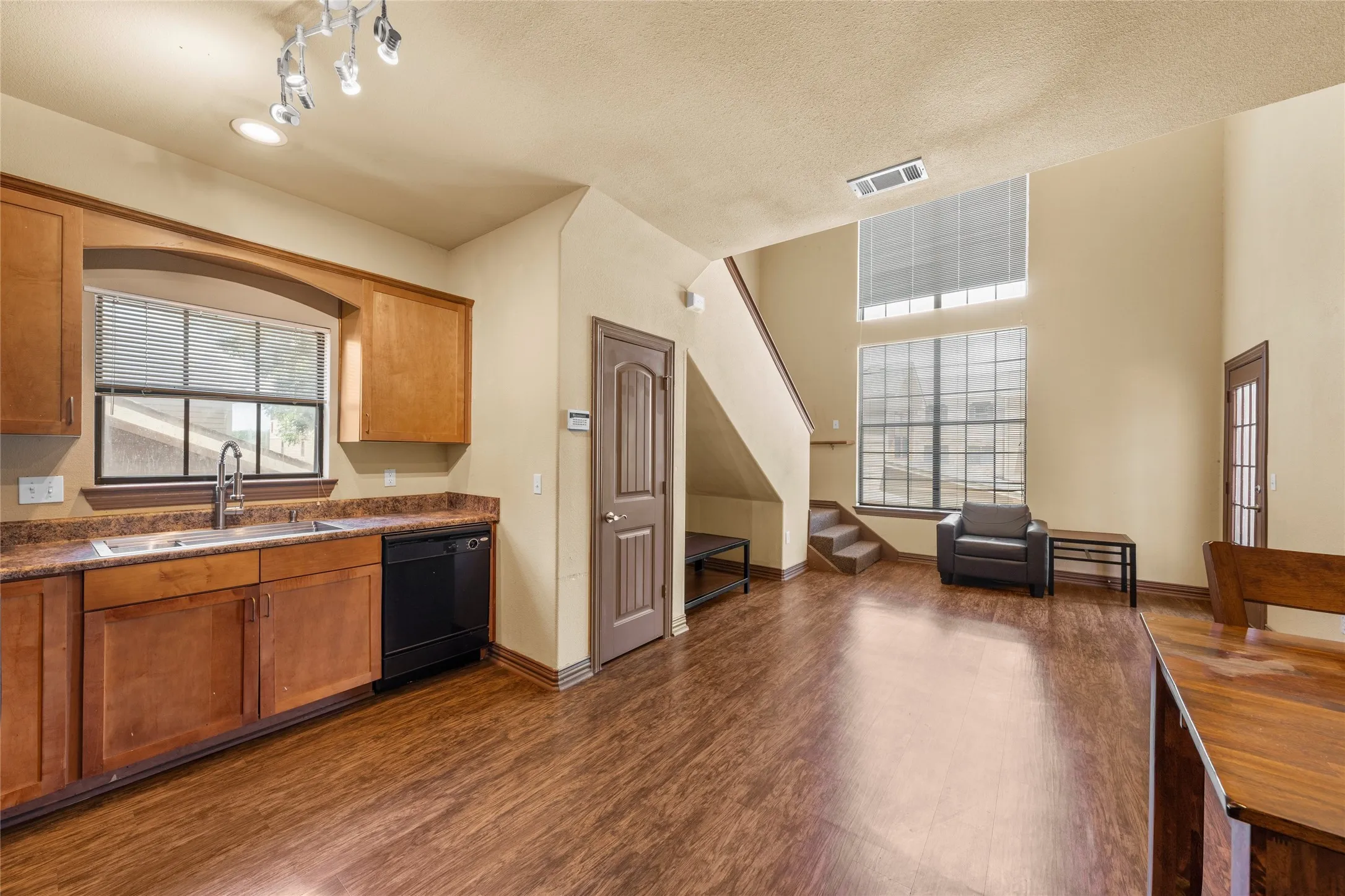 Open-concept living area featuring wood-finish flooring, a two-story ceiling, and a prominent staircase with a built-in bench