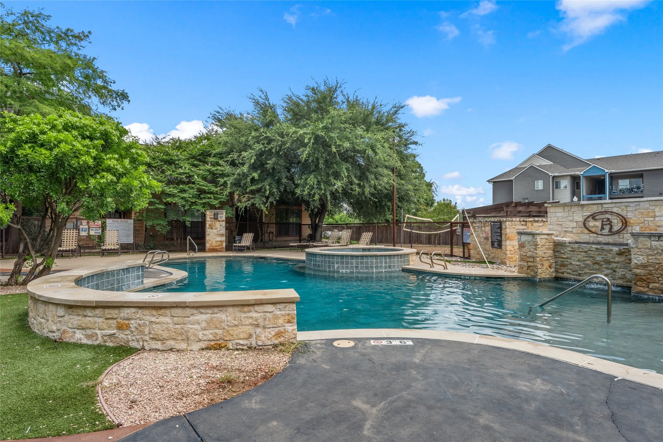 Resort-style swimming pool featuring a curved stone wall, integrated spa, and clear blue water
