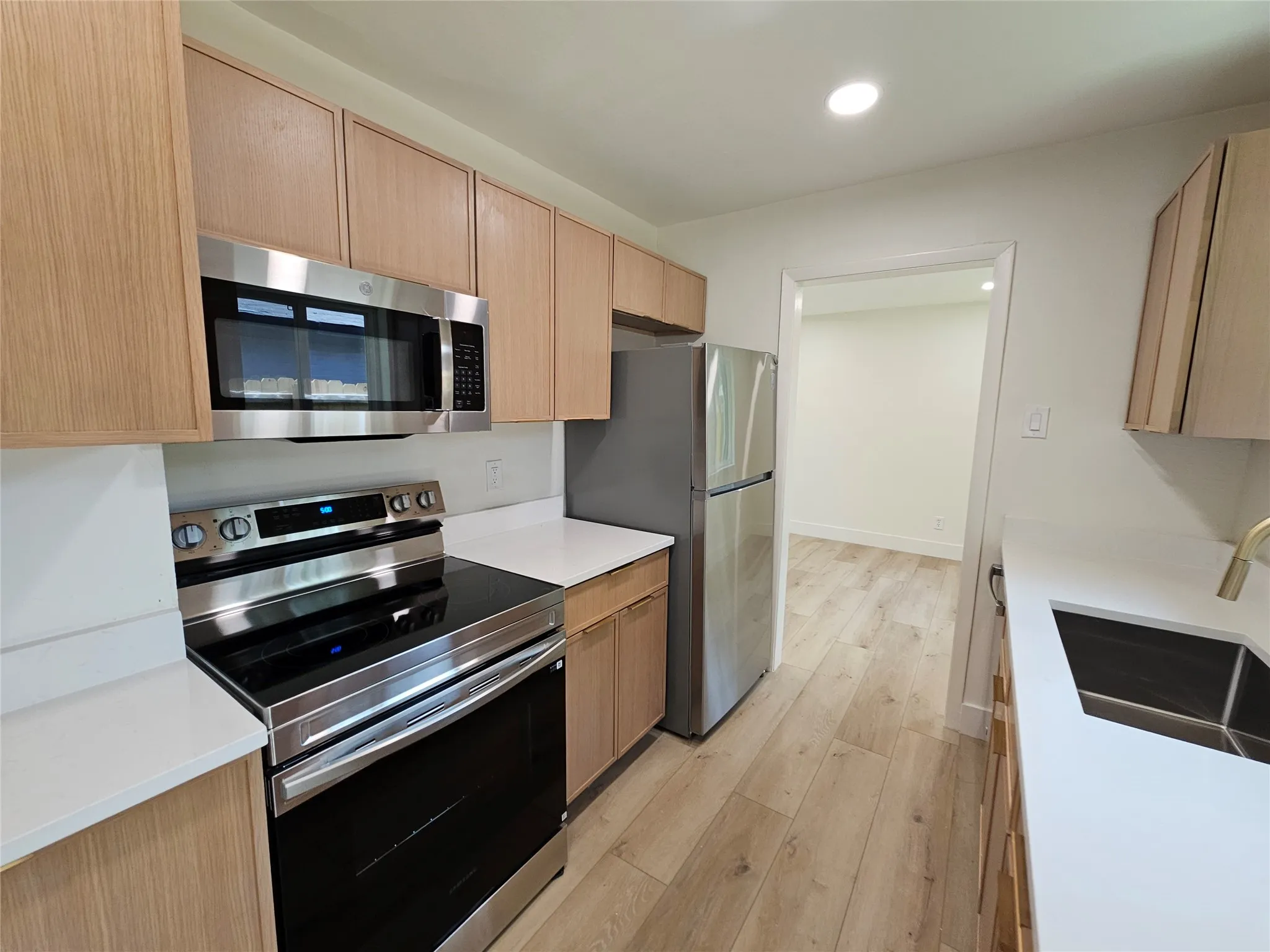 Kitchen featuring wood-finish cabinetry, stainless steel appliances, white countertops, and light wood-finish flooring