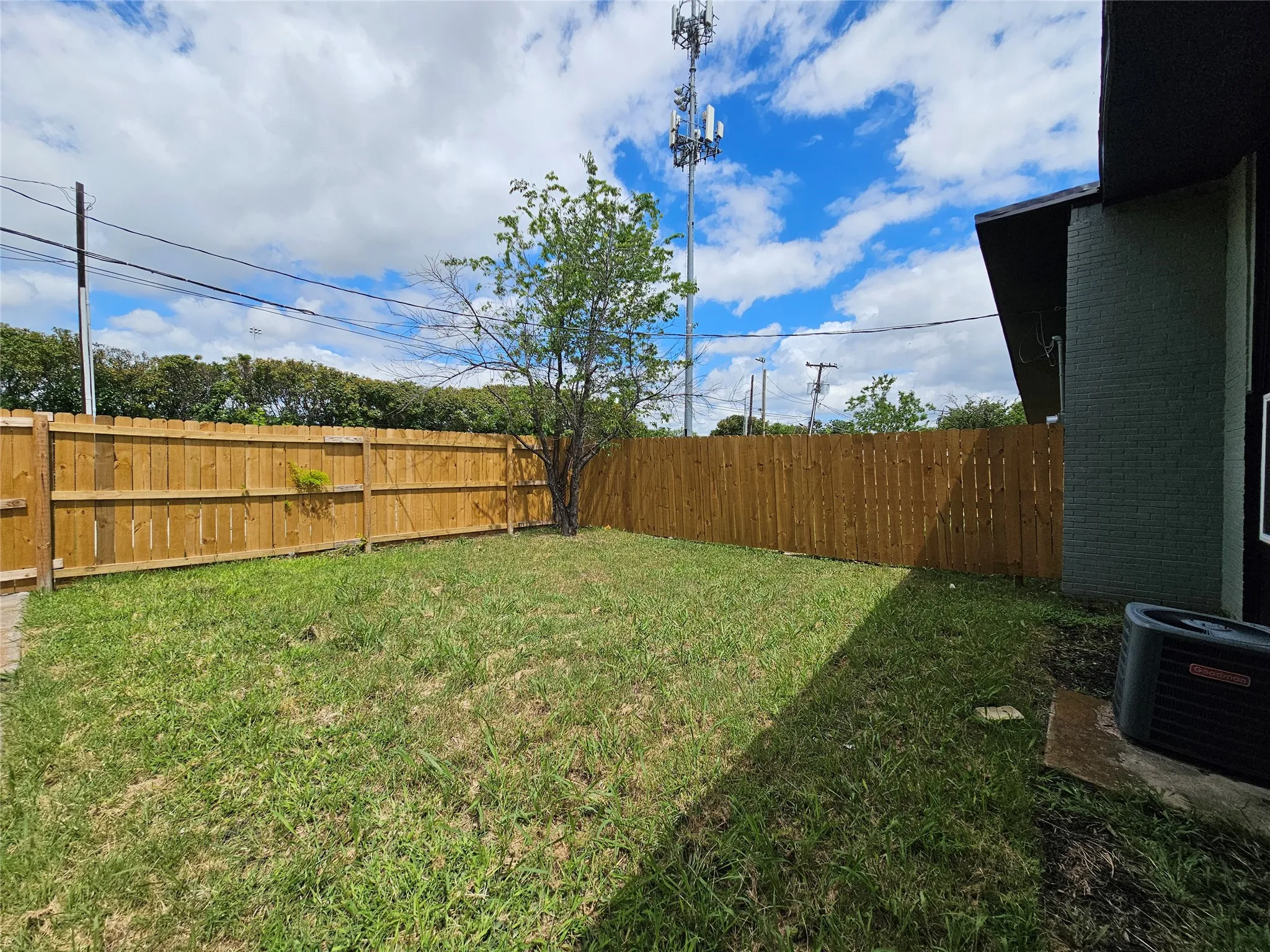 Private backyard space featuring a wooden privacy fence, a mature tree, and a grass lawn