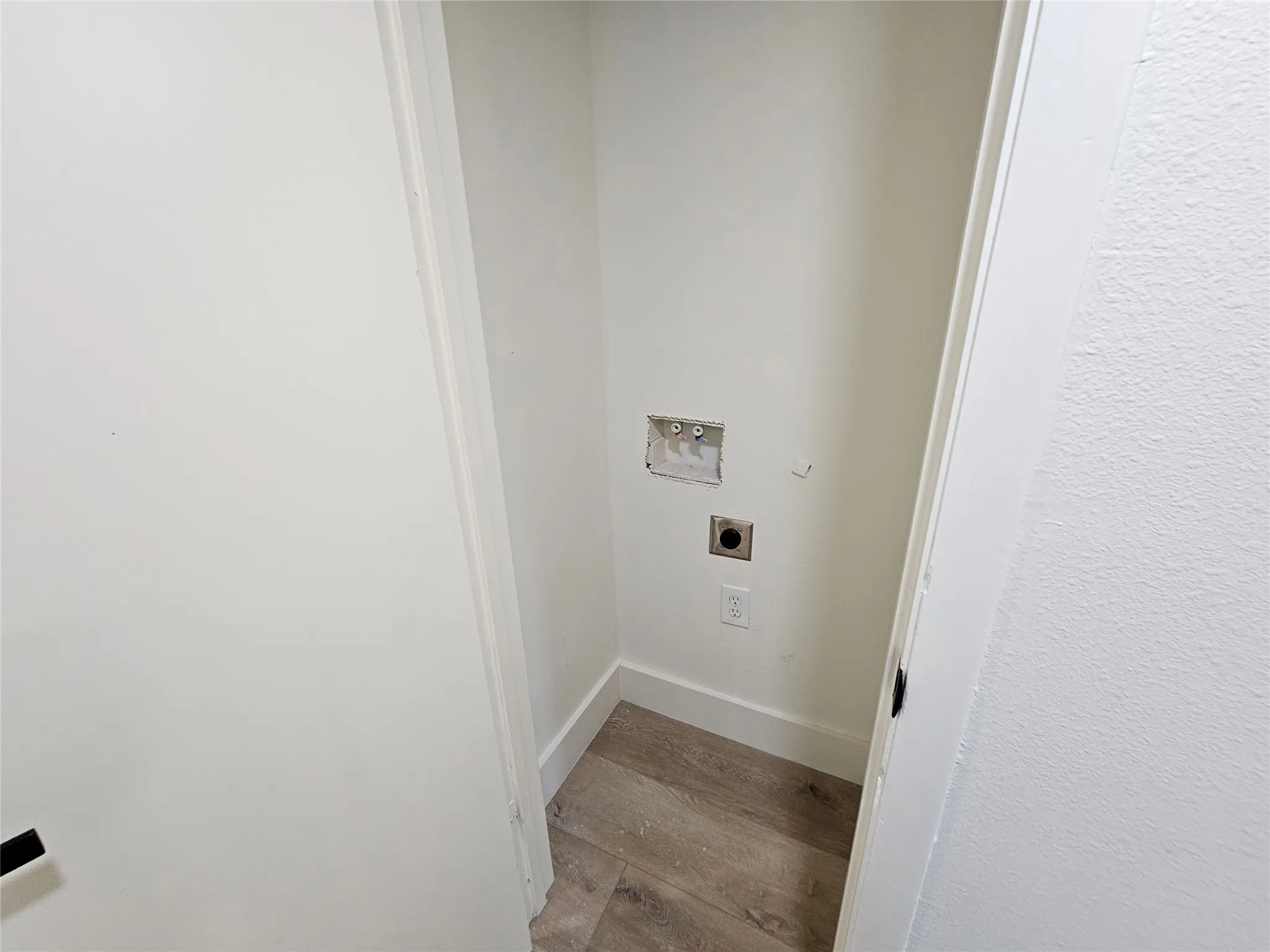 Dedicated laundry alcove featuring neutral white walls, white trim, wood-finish flooring, a wall-mounted dryer vent, and plumbing hookups