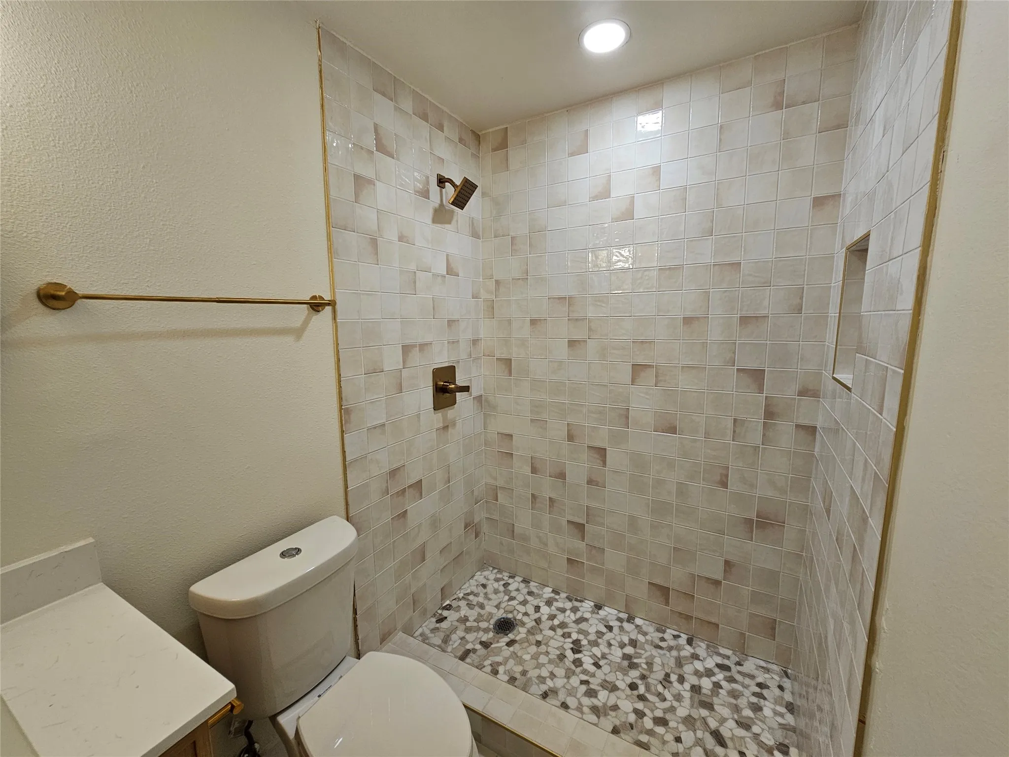 Walk-in shower featuring mosaic pebble flooring, tiled walls with an integrated niche, and bronze-finish fixtures