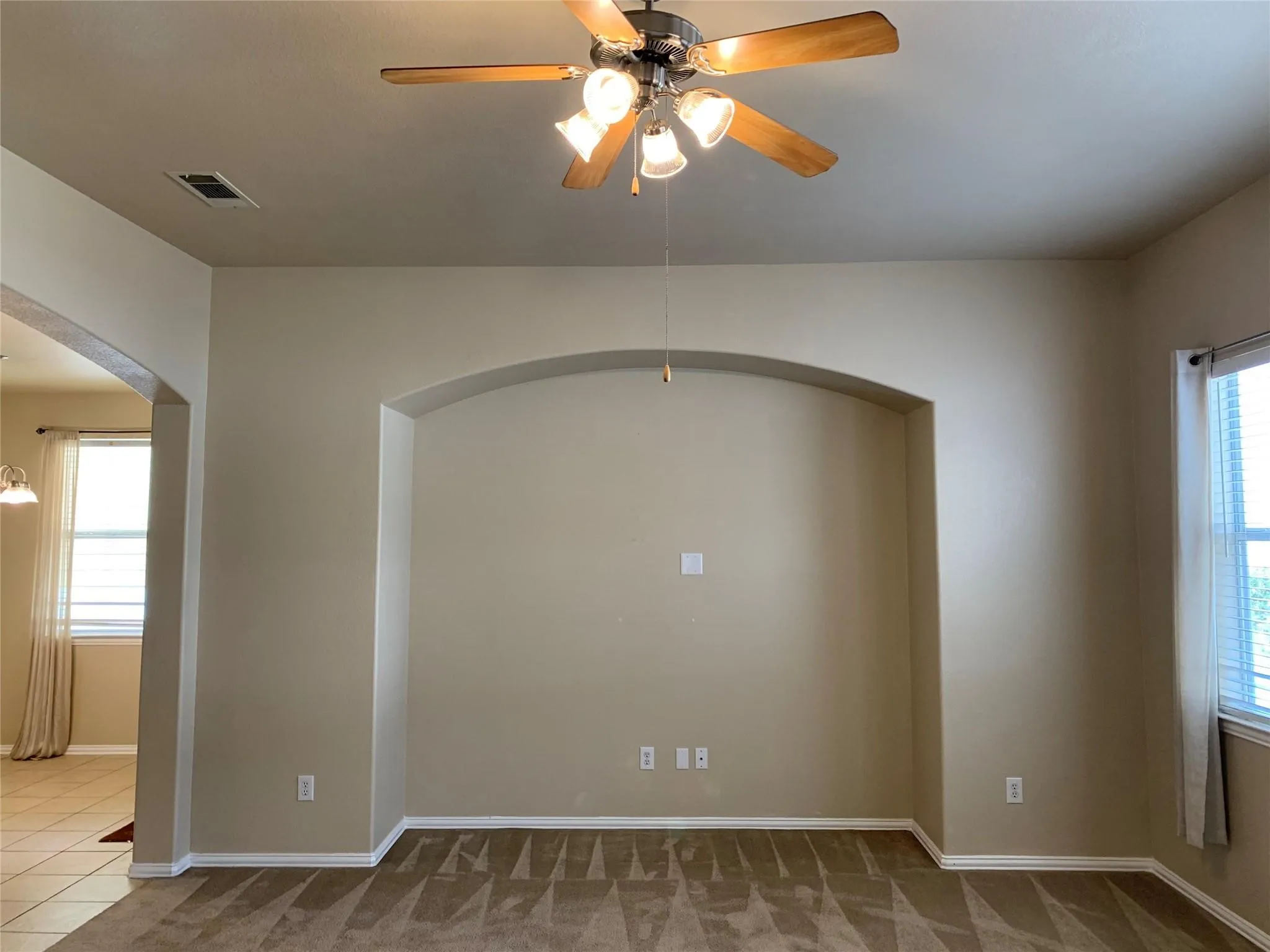 Spacious room featuring a decorative arched wall niche, a ceiling fan with integrated lighting, and neutral tone walls