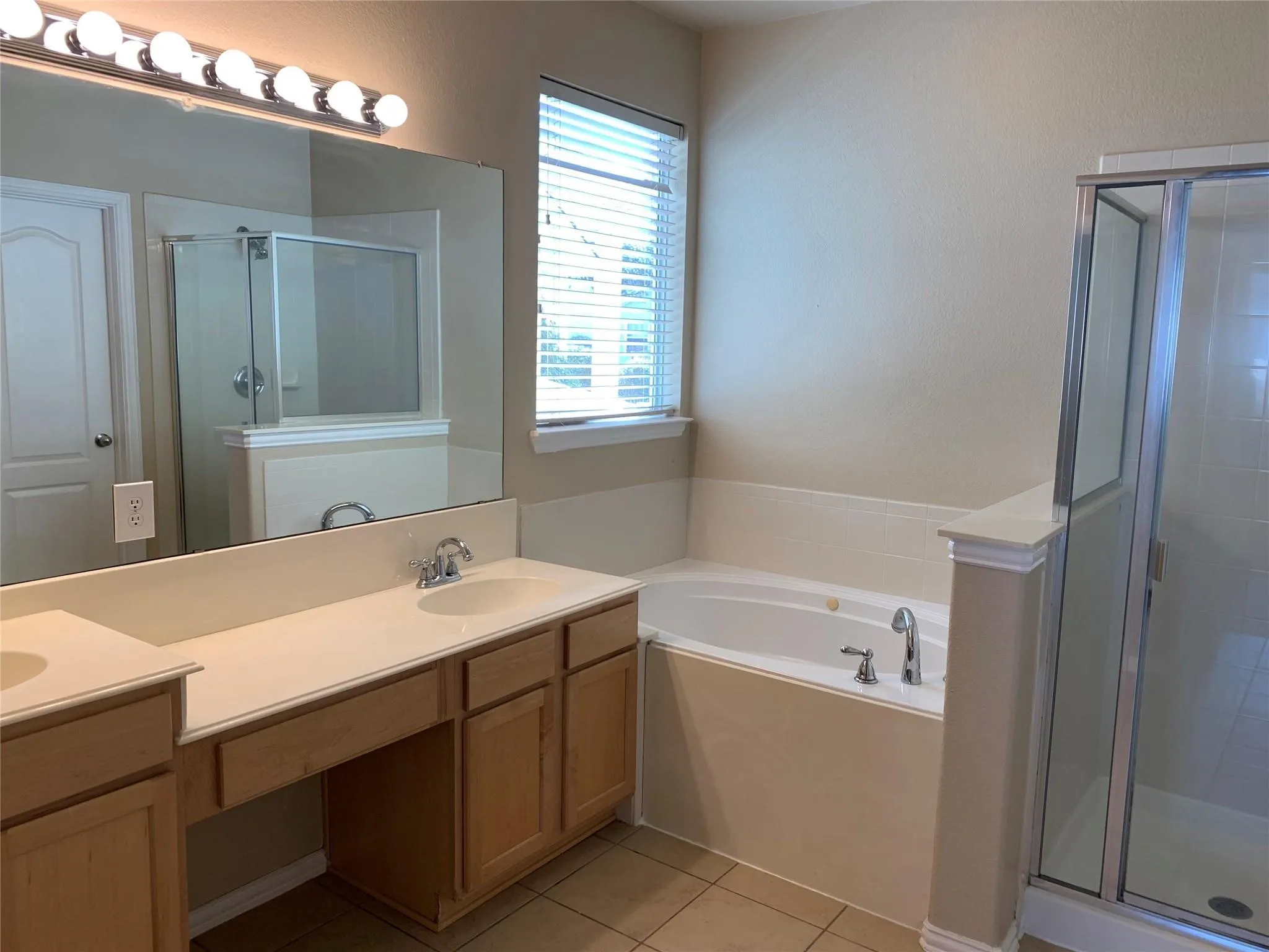 Bathroom featuring a dual vanity with light-tone cabinetry, a built-in garden tub, and a separate glass-enclosed shower