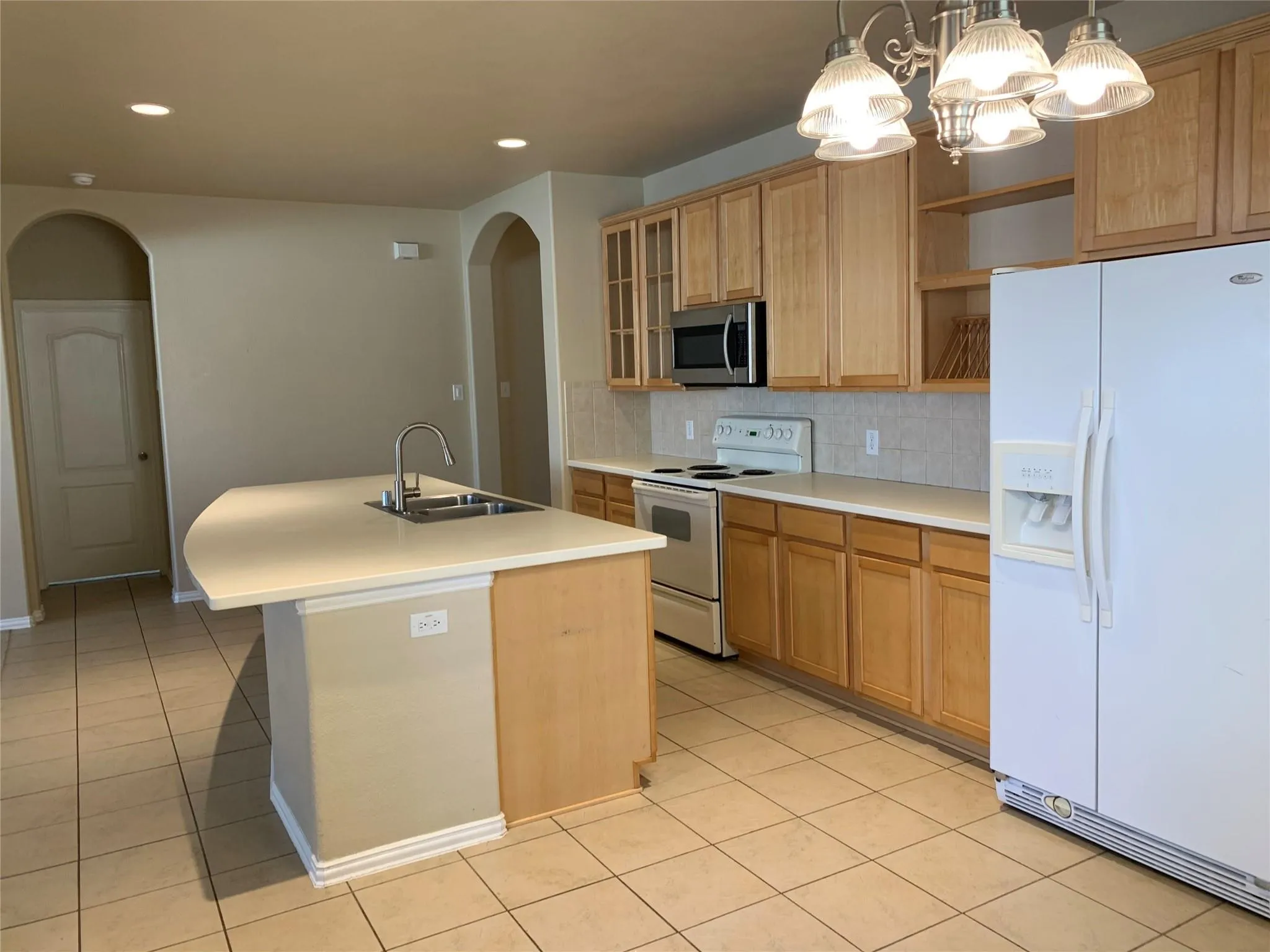 Kitchen featuring a central island with an integrated sink, light wood-finish cabinetry, tile flooring, and a subway tile backsplash