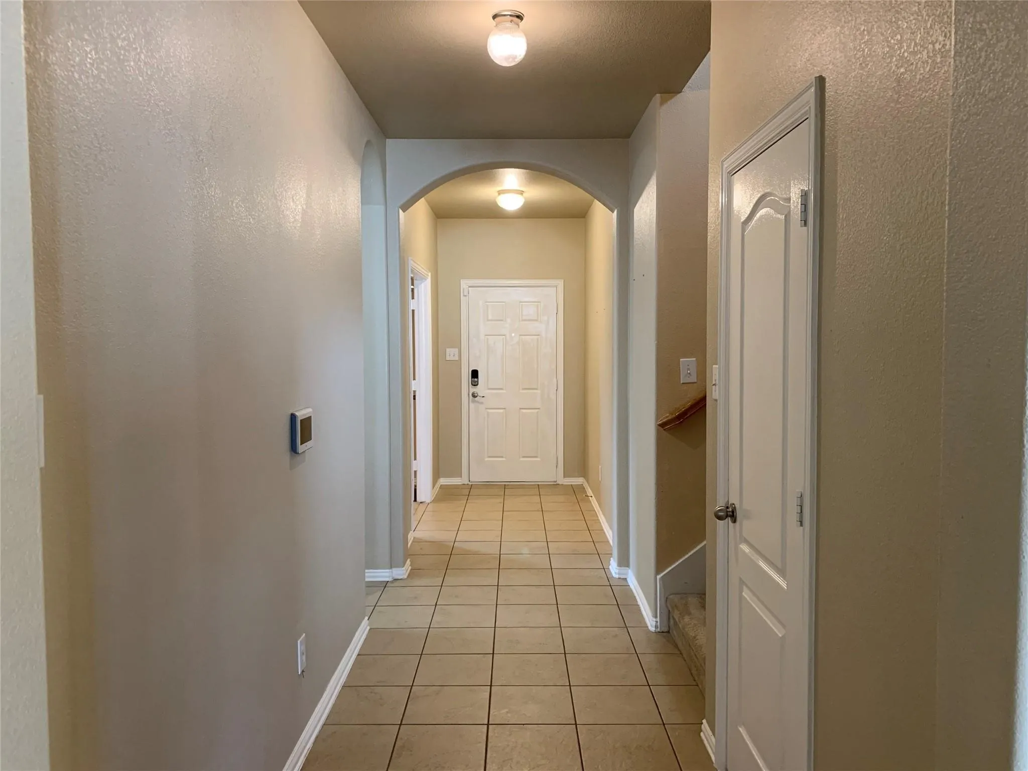 Foyer featuring tile flooring, neutral wall tones, arched entryway, and a white paneled door