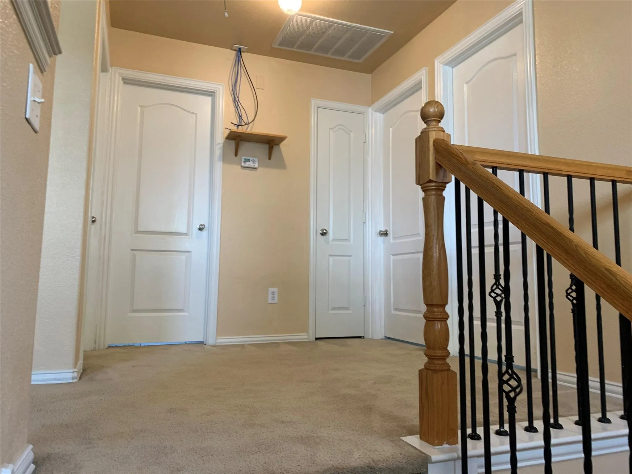 Carpeted landing with white baseboards, multiple panel doors, and a wood handrail with wrought iron balusters