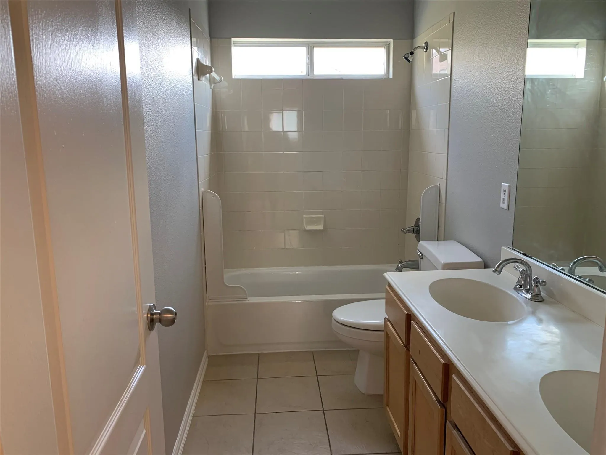 Bathroom featuring a dual-sink vanity with wood-finish cabinetry, a full-width mirror, and a bathtub with tile surround