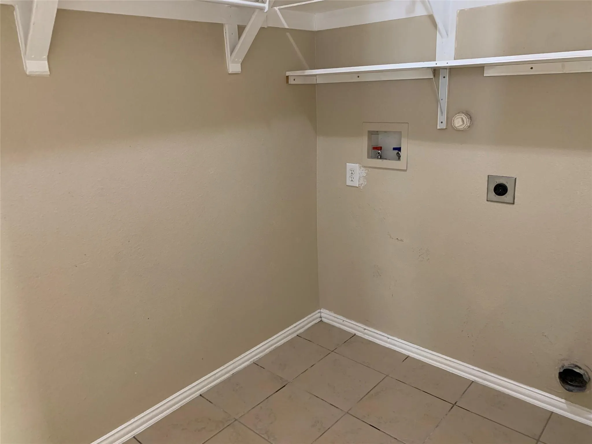 Utility space featuring a tile floor, base molding, light beige wall paint, and white shelving