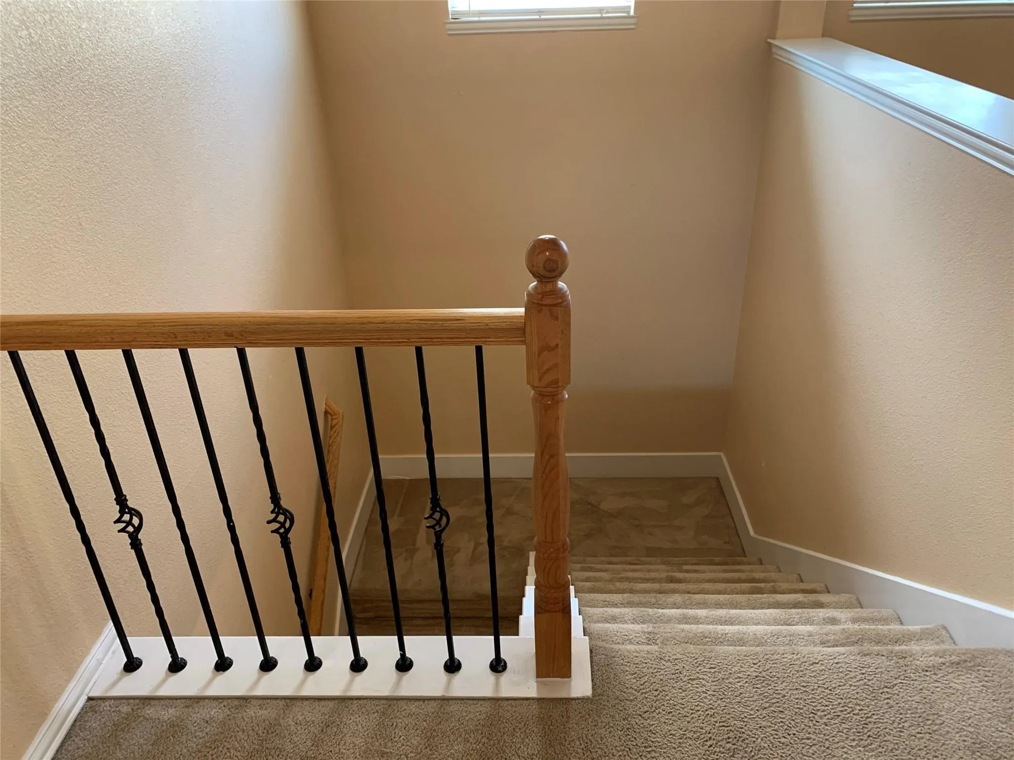 Staircase featuring wood-finish handrail, decorative wrought iron balusters, and carpeted treads
