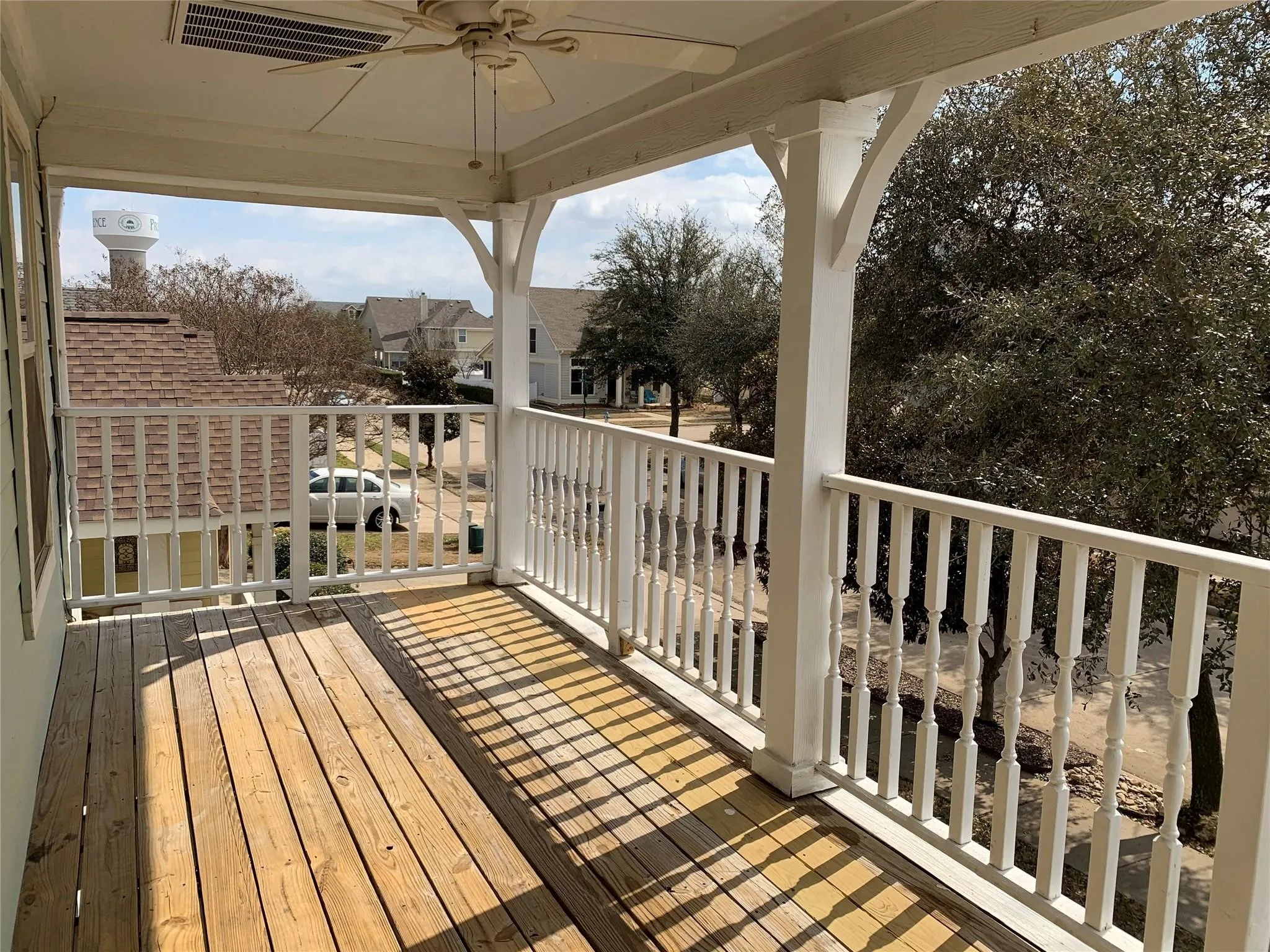 Expansive covered porch featuring wood-finish flooring, white baluster railing, and a ceiling fan