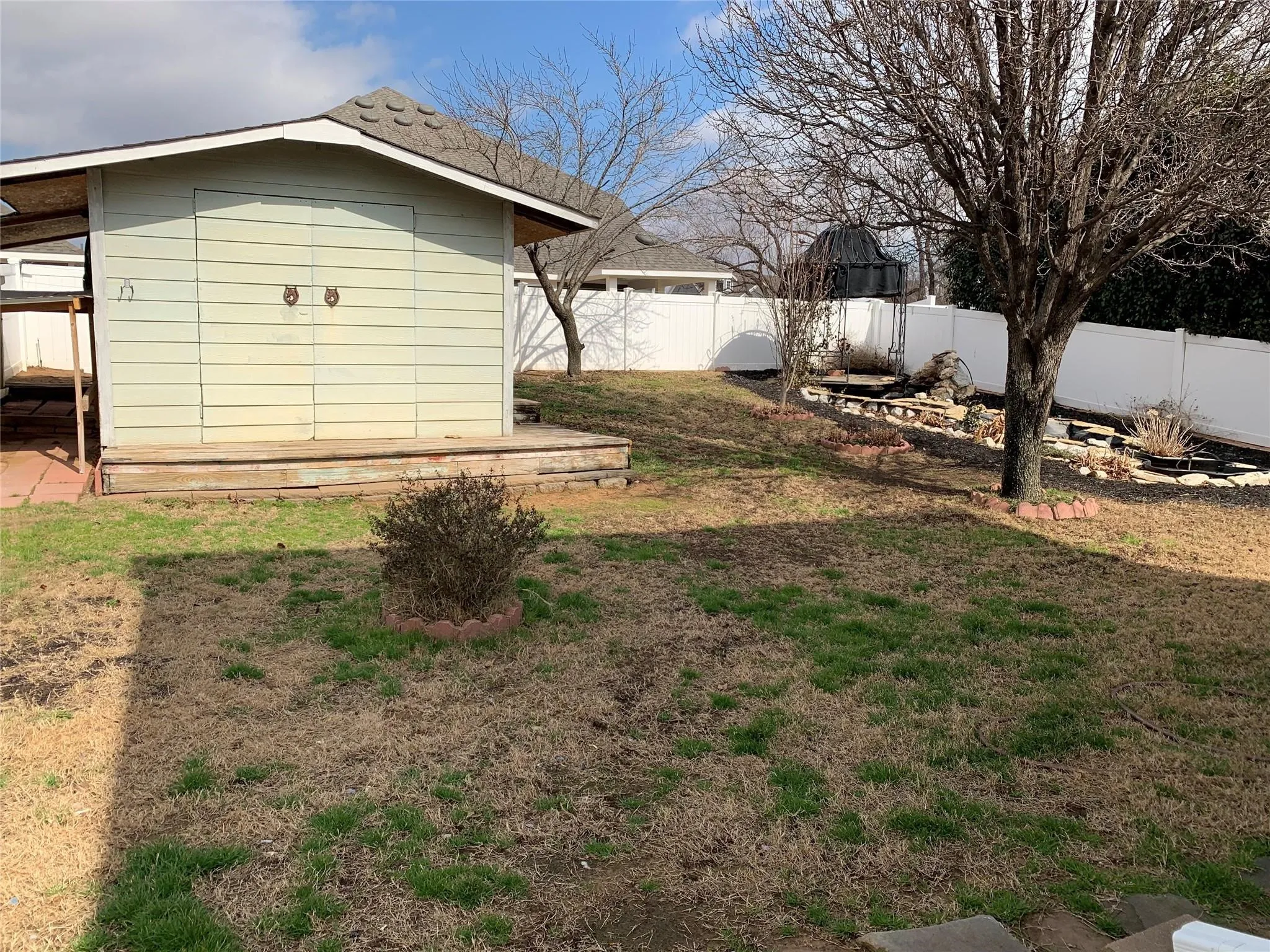Expansive backyard featuring a storage shed with a shingled roof, a stepped wooden porch, and double doors with decorative hardware