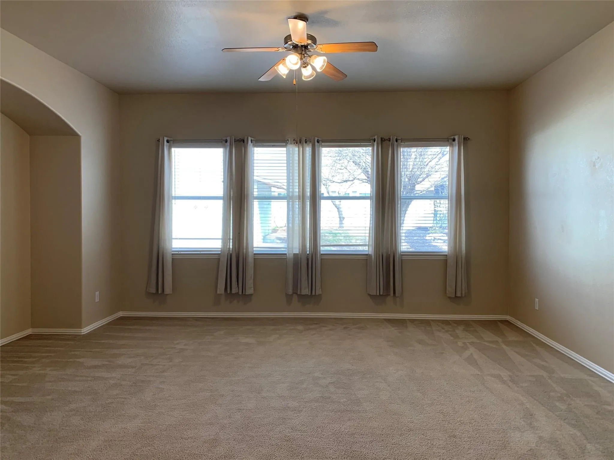 Spacious interior room featuring four large windows, neutral-toned walls, and a ceiling fan with integrated lighting
