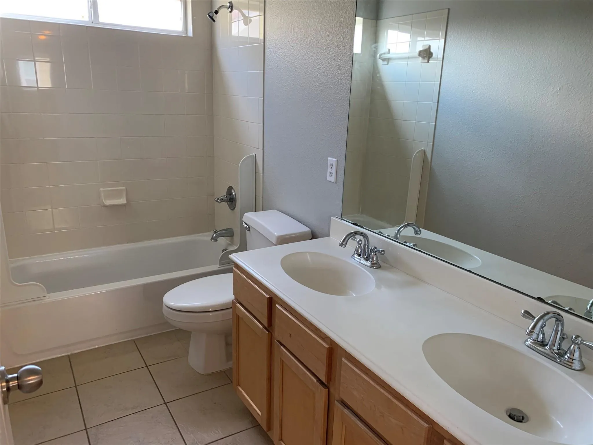 Bathroom featuring a dual vanity with light wood cabinetry, a built-in mirror, and a combination tub/shower with white tile surround