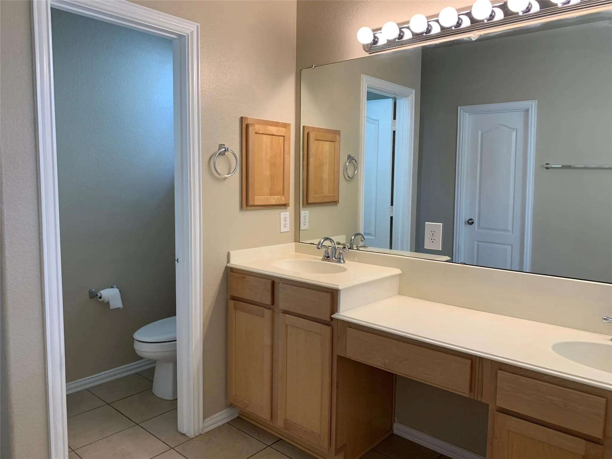 Bathroom featuring a dual vanity with light-toned cabinetry, a built-in makeup counter, and a large wall-mounted mirror with overhead bar lighting