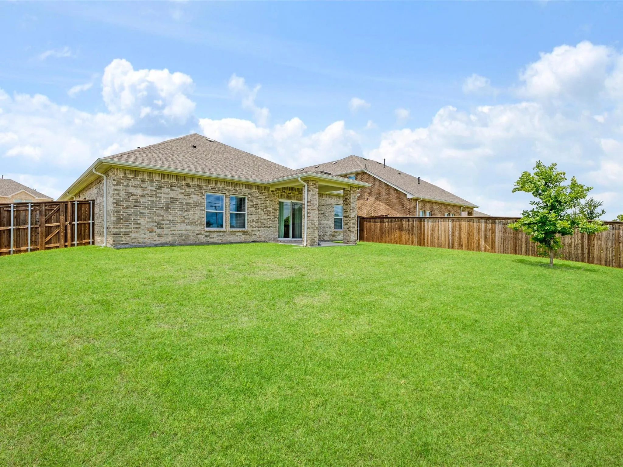 Expansive backyard featuring a lush lawn, a mature tree, a full privacy fence, and a covered patio with direct access to the interior