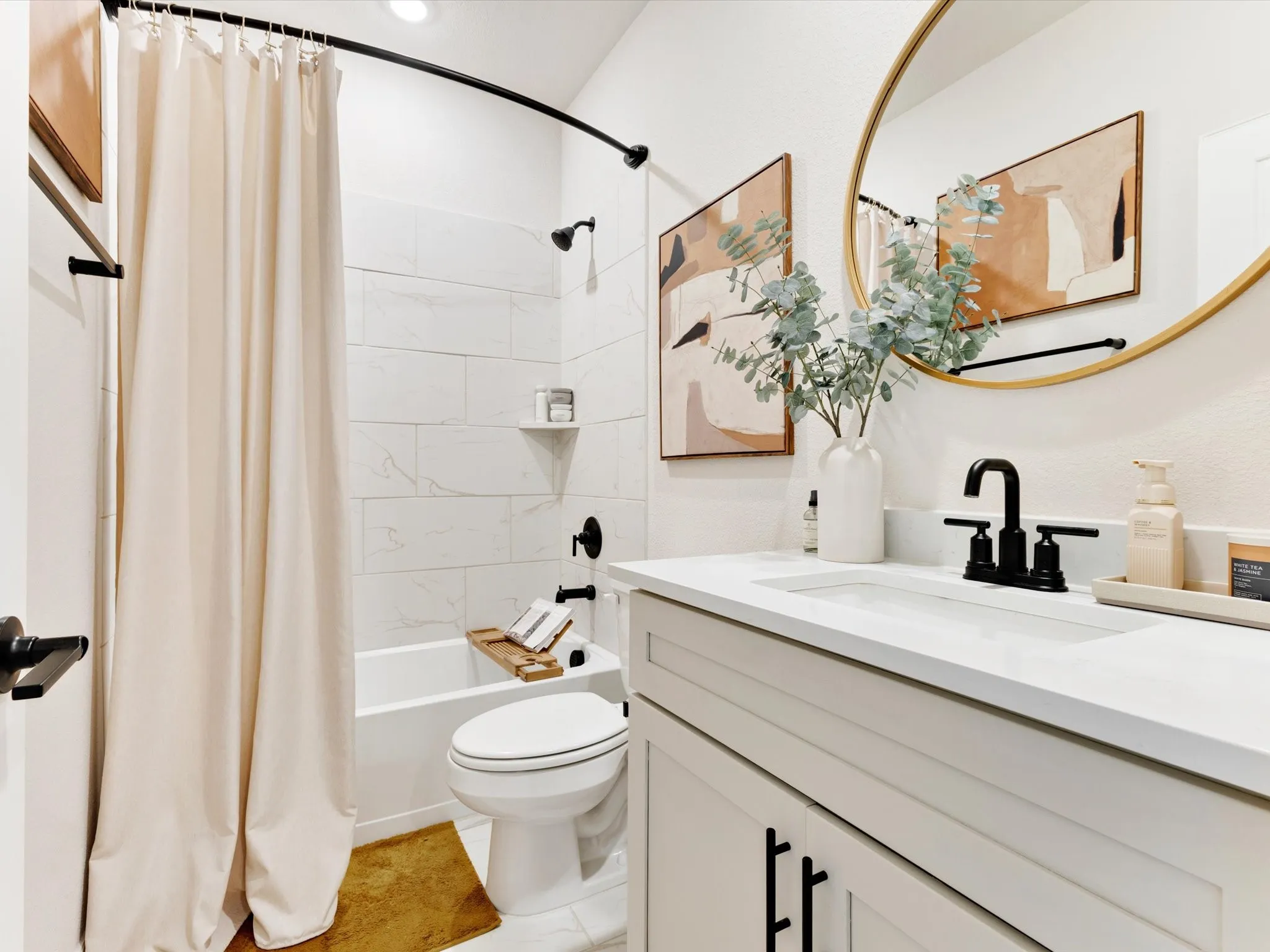 Bathroom featuring a white vanity with a rectangular integrated sink, matte black faucet, and a round gold-framed mirror