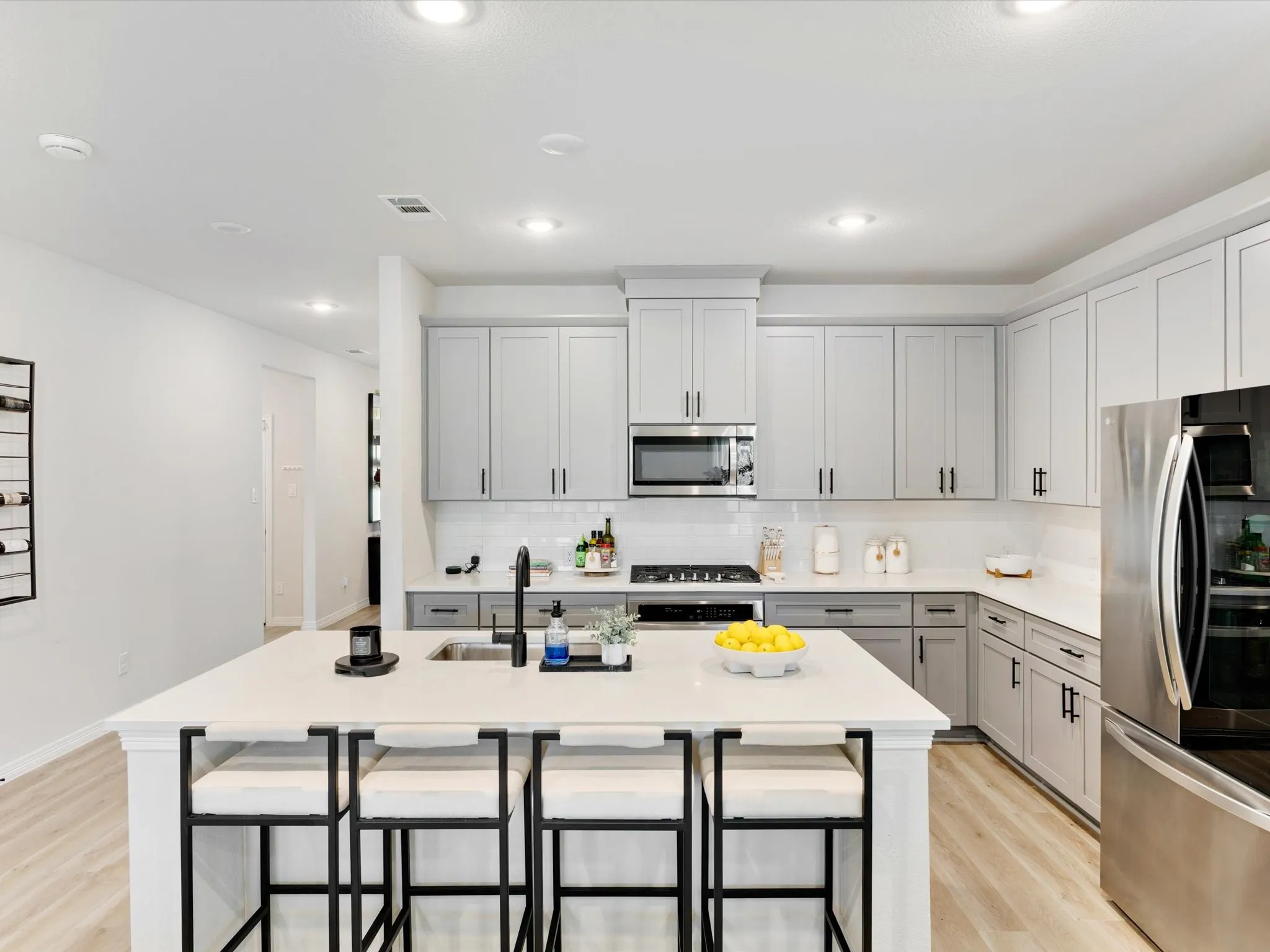 Contemporary kitchen featuring a large center island with integrated sink, stainless steel appliances, light gray cabinetry, and wood-finish flooring
