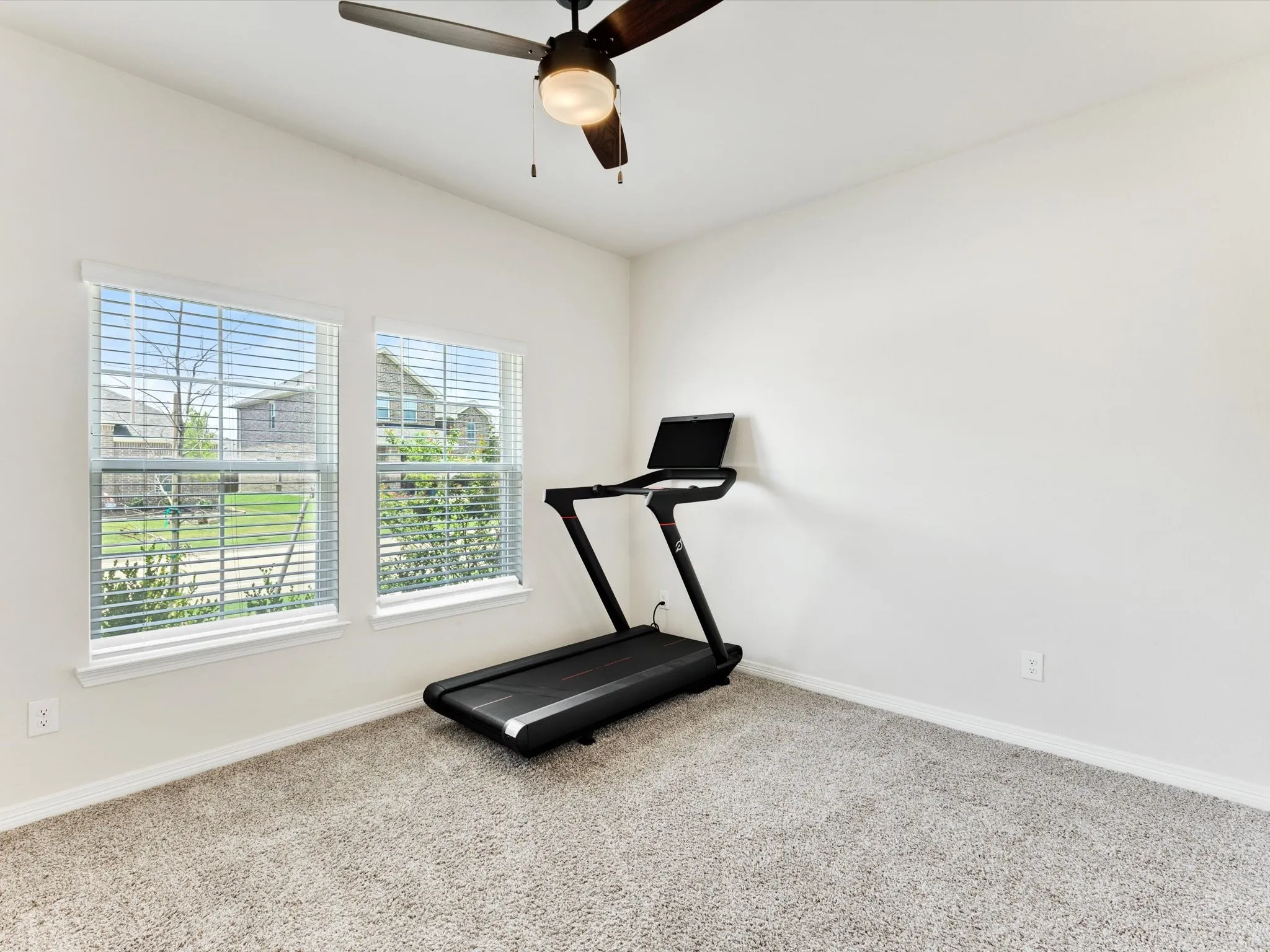 Room featuring dual windows with blinds, light-toned carpeting, and a ceiling fan with integrated lighting