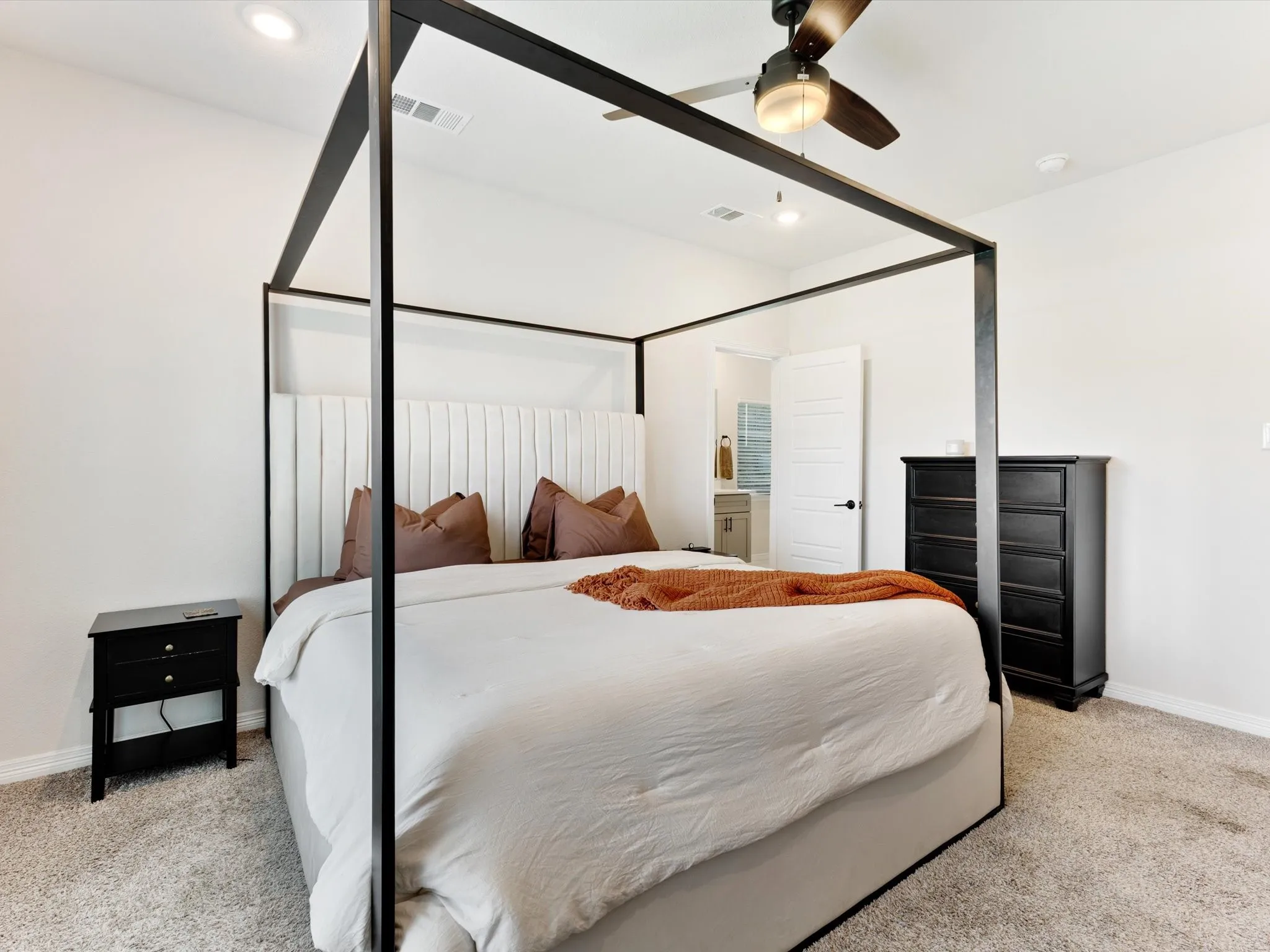 Recessed lighting, ceiling fan, plush carpet flooring, white paneled door, and a glimpse of an en-suite bathroom