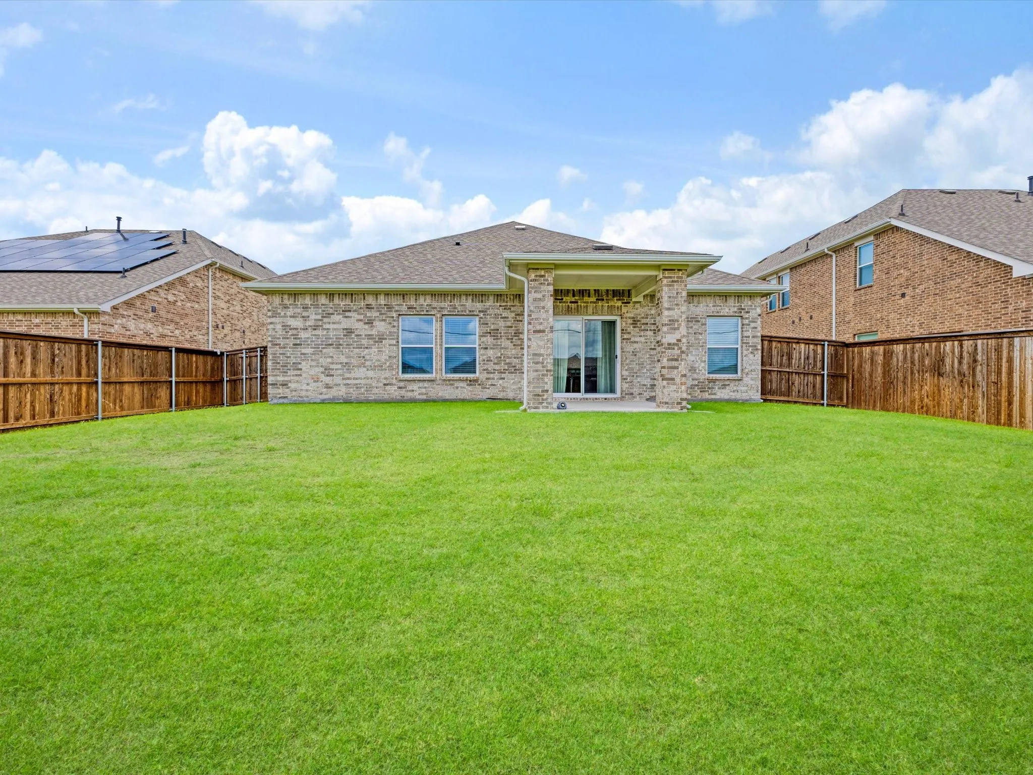 Expansive green lawn surrounds a brick exterior home with a covered patio