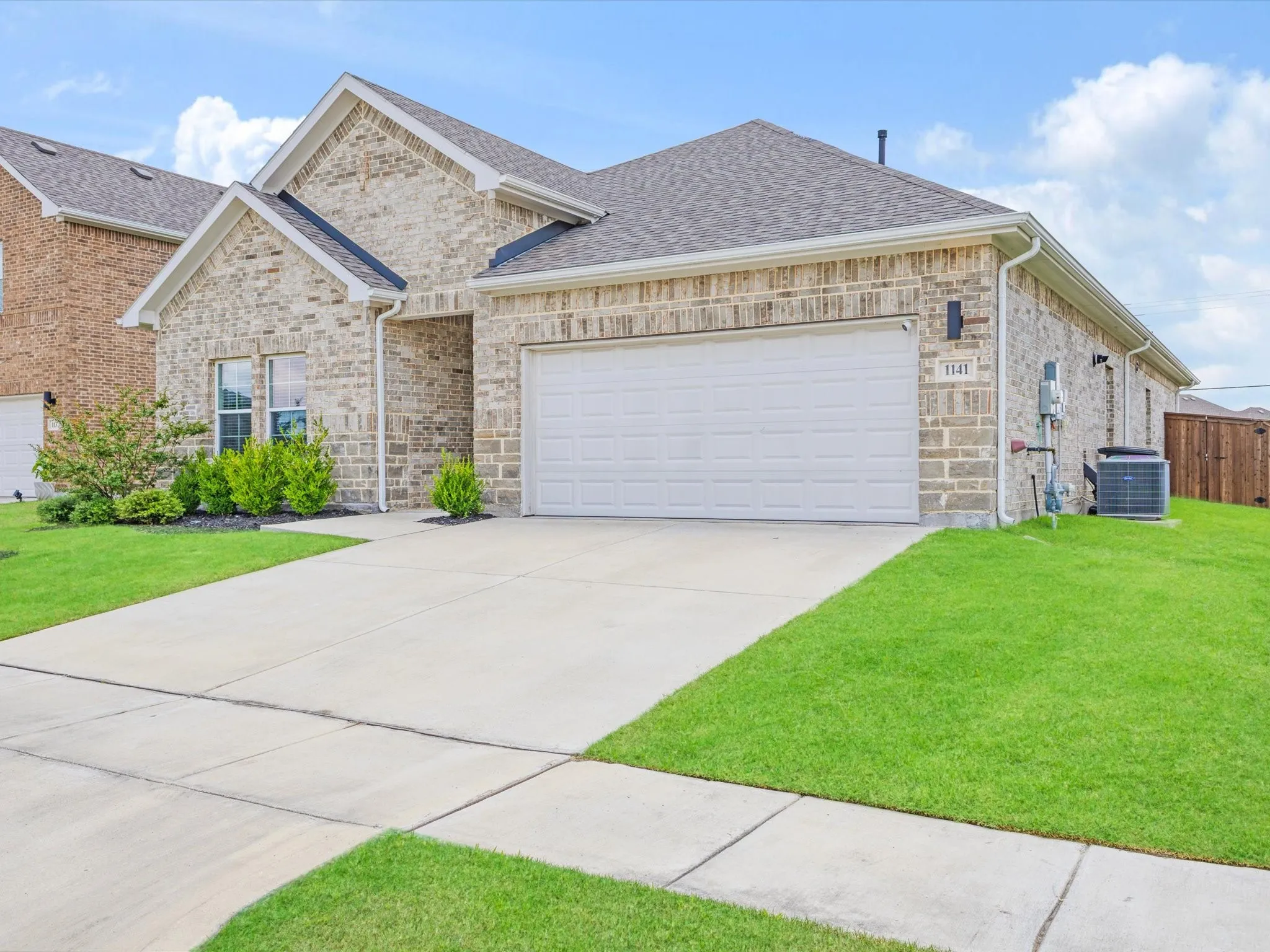 Brick exterior with a gabled roofline, featuring an attached garage with a white door and a concrete driveway