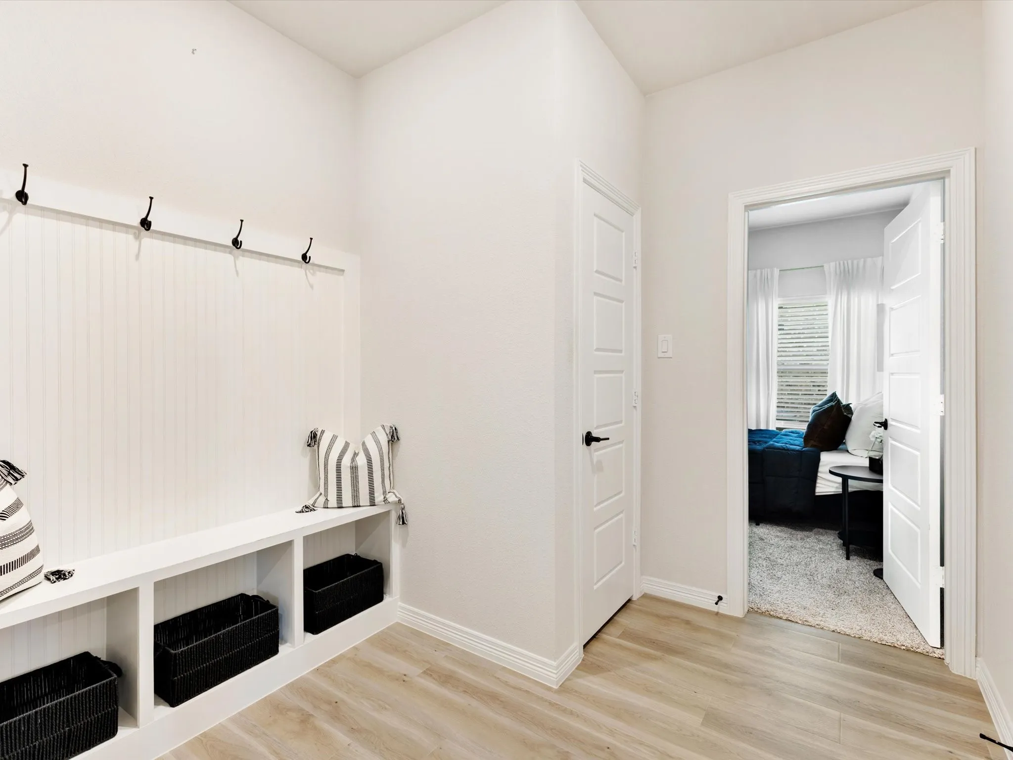 Entryway featuring a built-in bench with integrated storage cubbies and coat hooks, wood-finish flooring, white paneled walls, and white trim