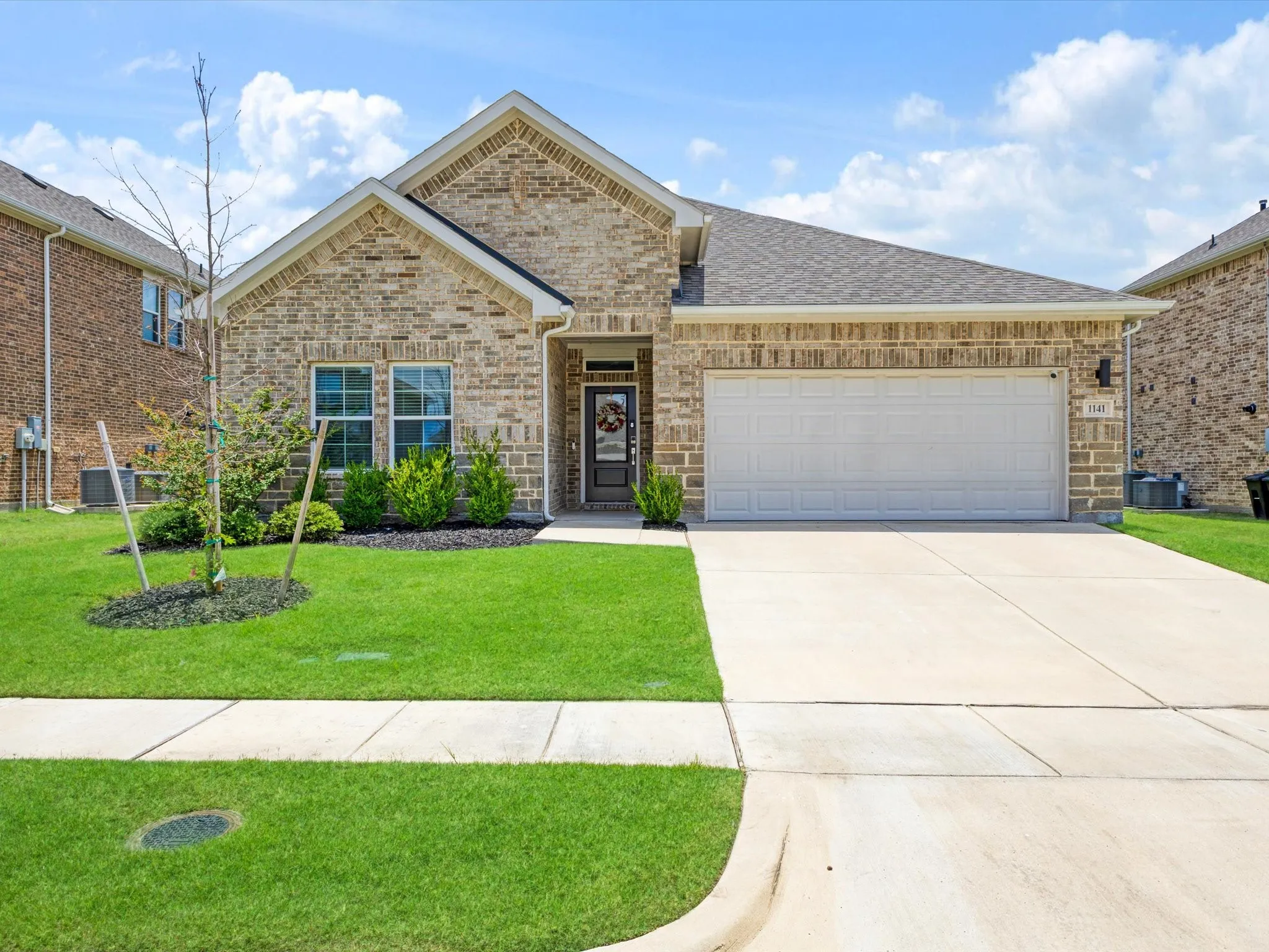 Brick facade home with an attached garage, landscaped front yard, and concrete driveway
