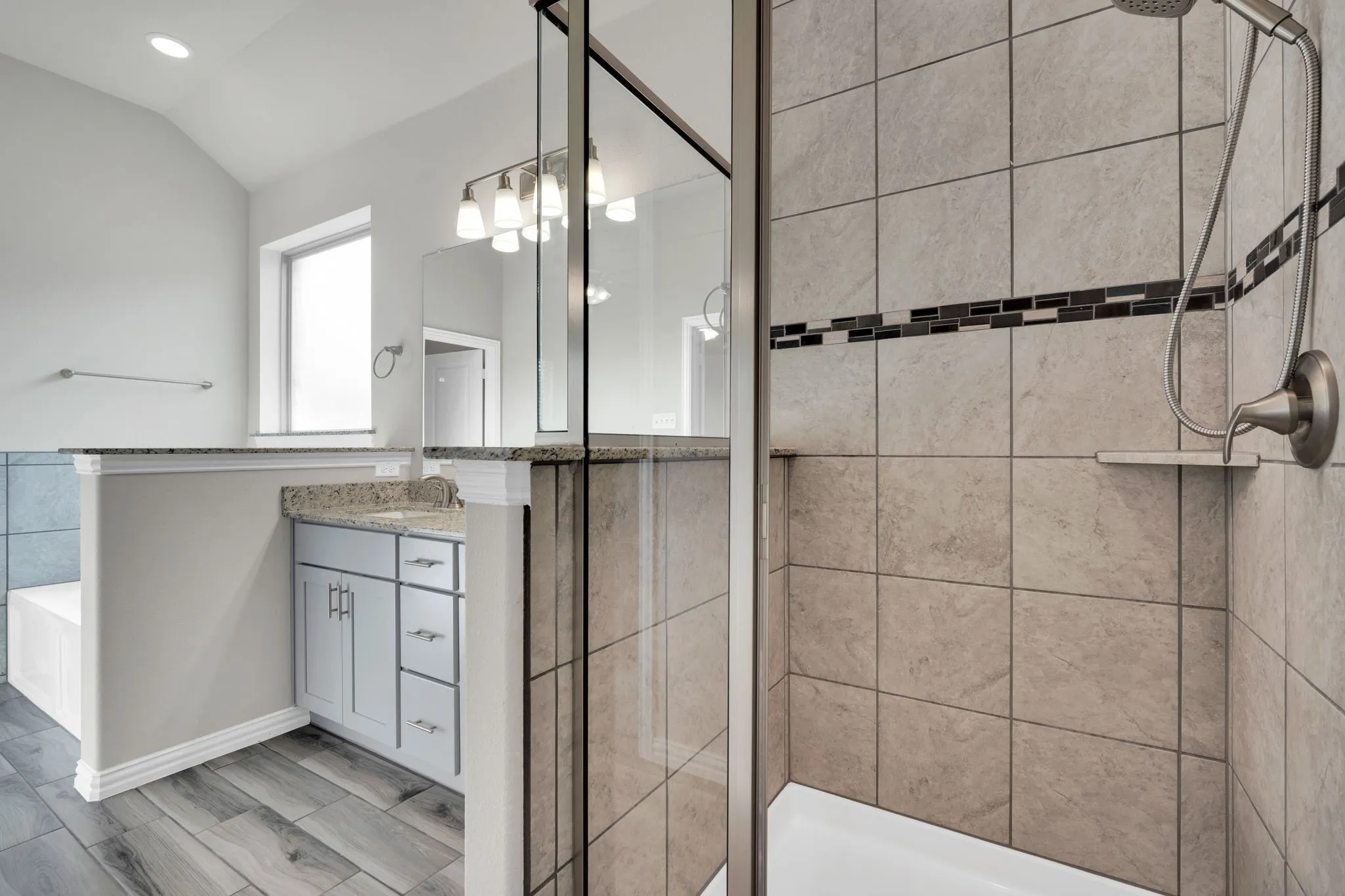 Enclosed shower with large format tile and decorative mosaic accent