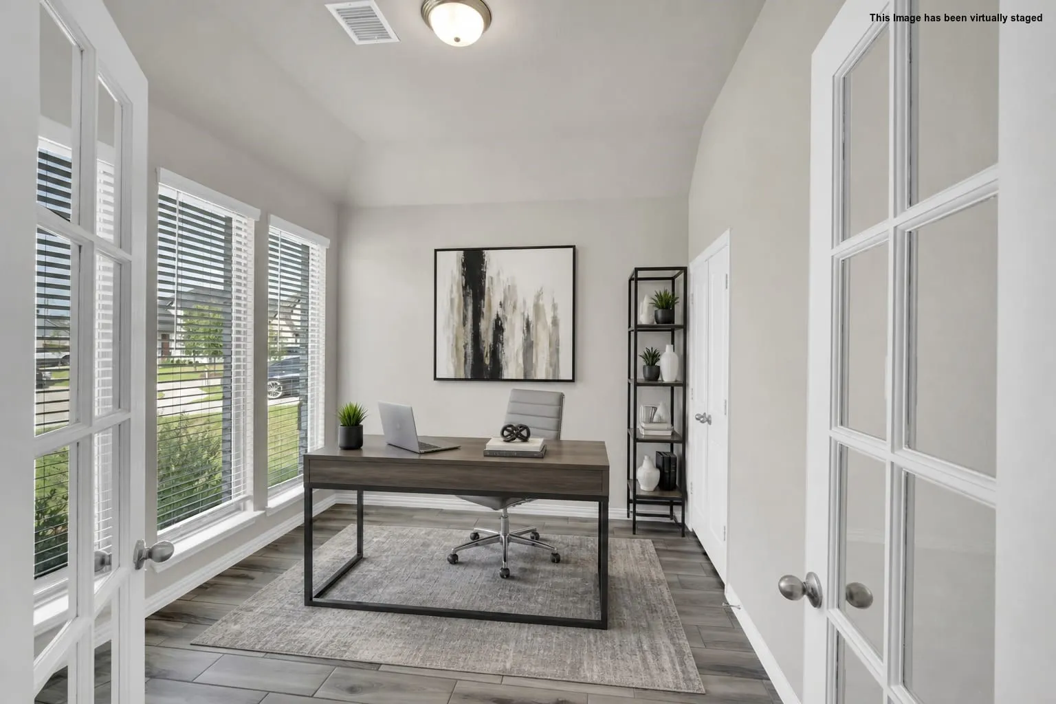 Spacious room featuring French doors, multiple windows with blinds, wood-finish flooring, and a vaulted ceiling with a flush-mount light fixture. Virtual Staged.