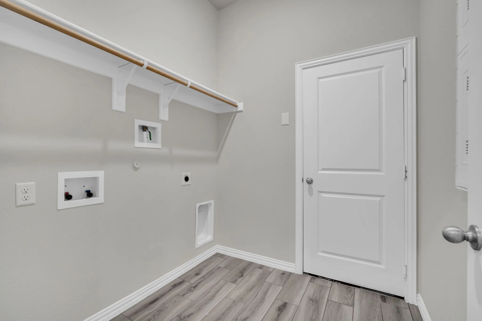 Dedicated laundry area featuring wood-finish flooring, light grey wall paint, and white baseboards