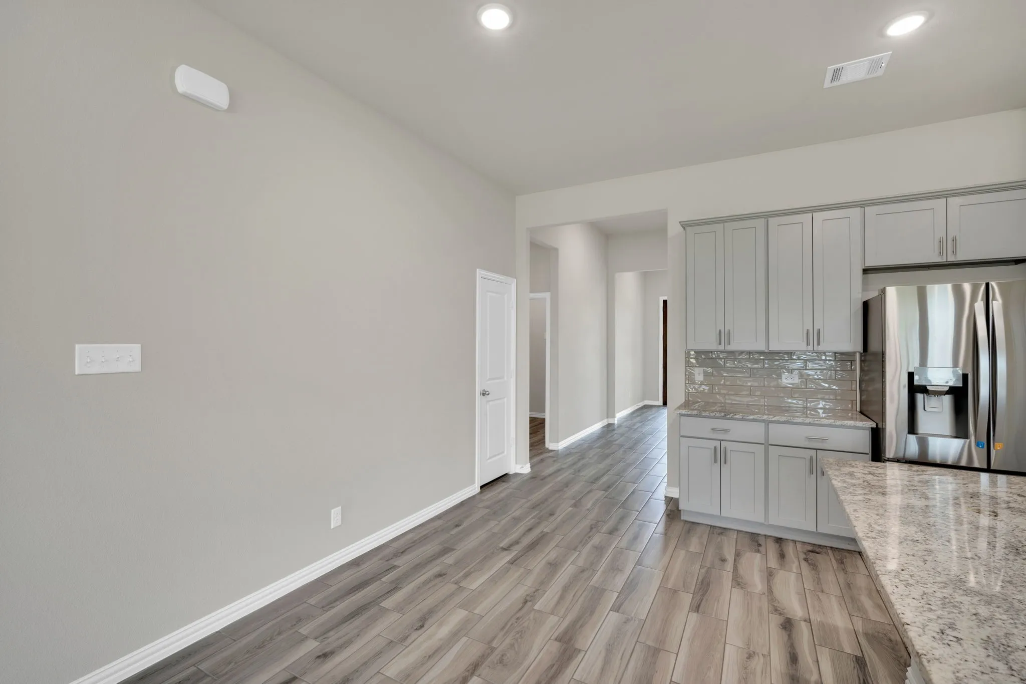 Spacious interior room featuring wood-finish flooring, ample natural light from multiple windows with blinds, a ceiling fan, recessed lighting, and a glass-paneled door
