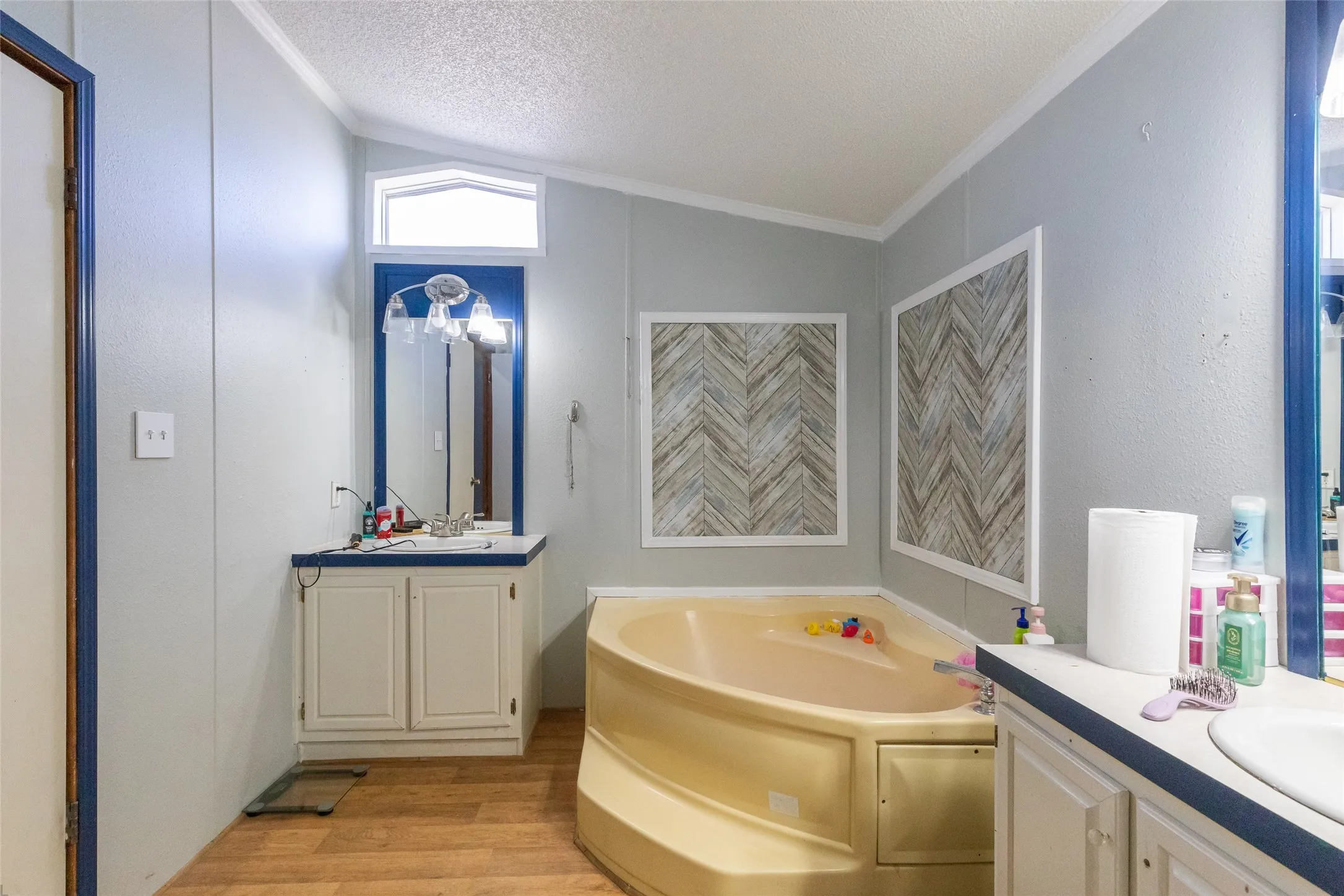 Bathroom featuring a corner soaking tub, two separate vanity sinks with cabinet storage, and wood-finish flooring
