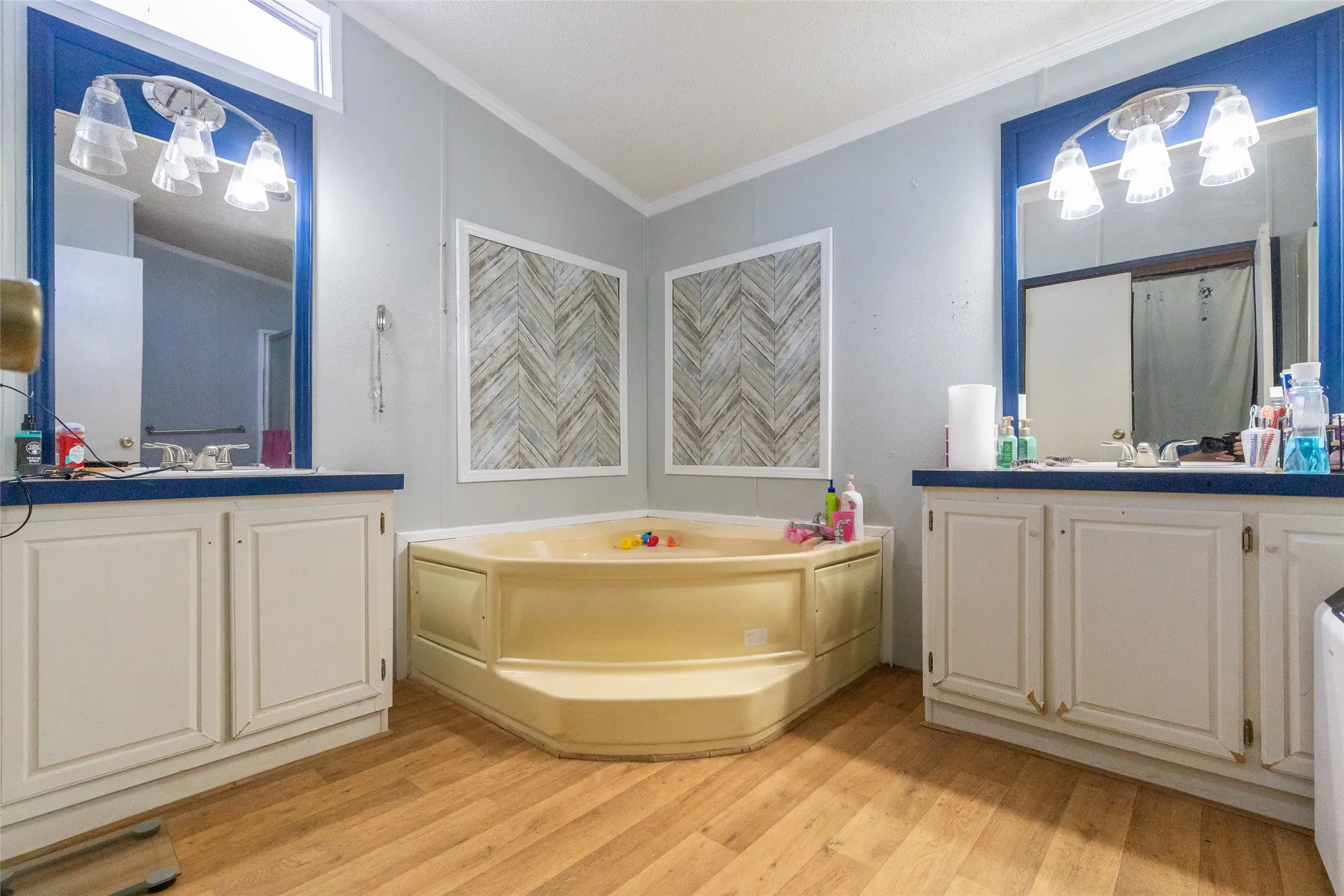 Bathroom featuring a corner soaking tub, dual vanity sinks, wood-finish flooring, and decorative accent panels