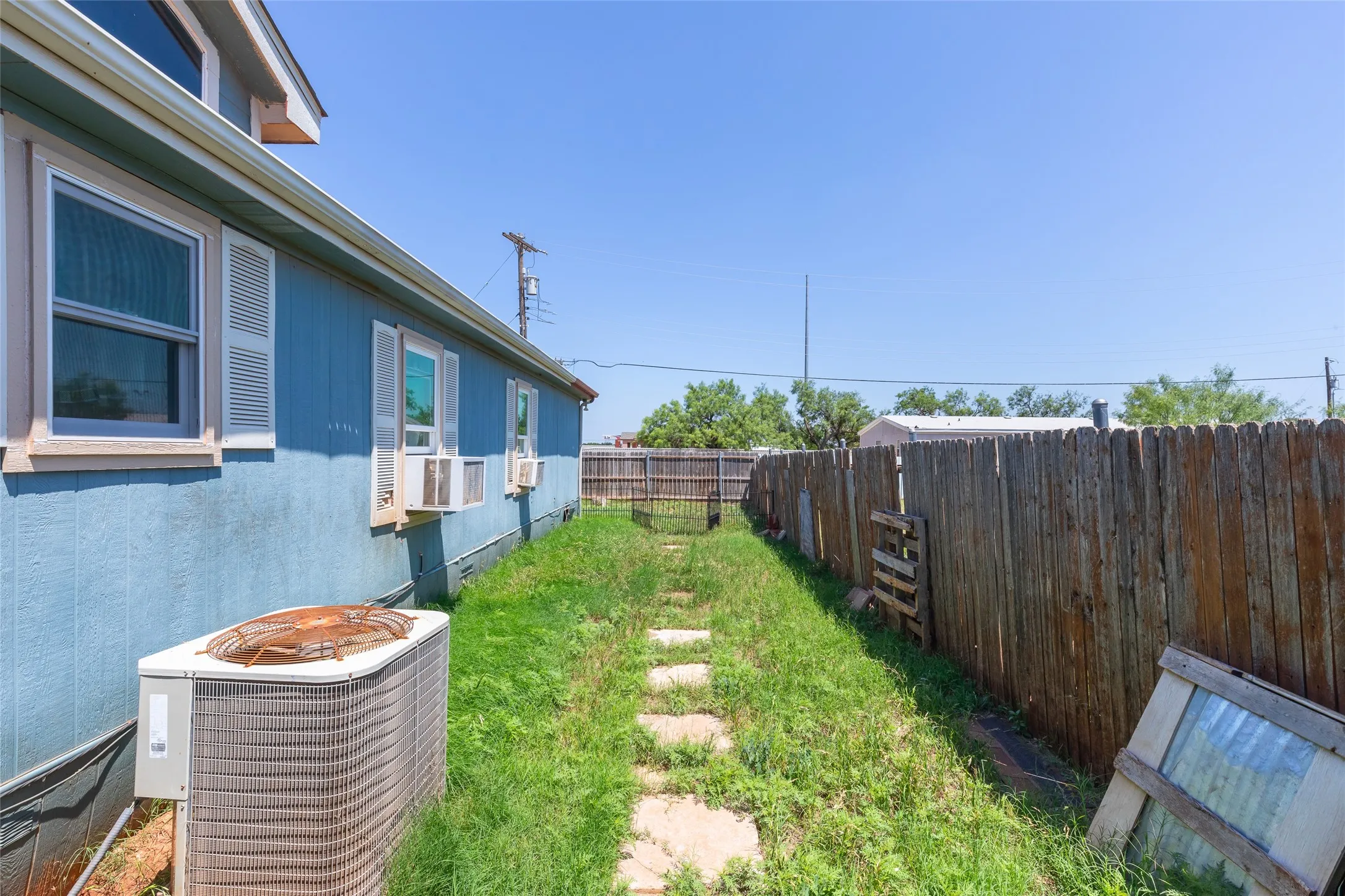 Side yard featuring a wooden privacy fence, stone pathway, and blue exterior siding