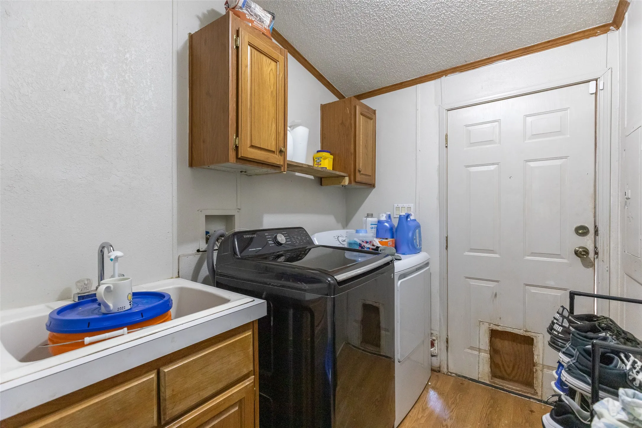 Utility room featuring wood-finish flooring, a white utility sink, wood cabinetry, and a white paneled door