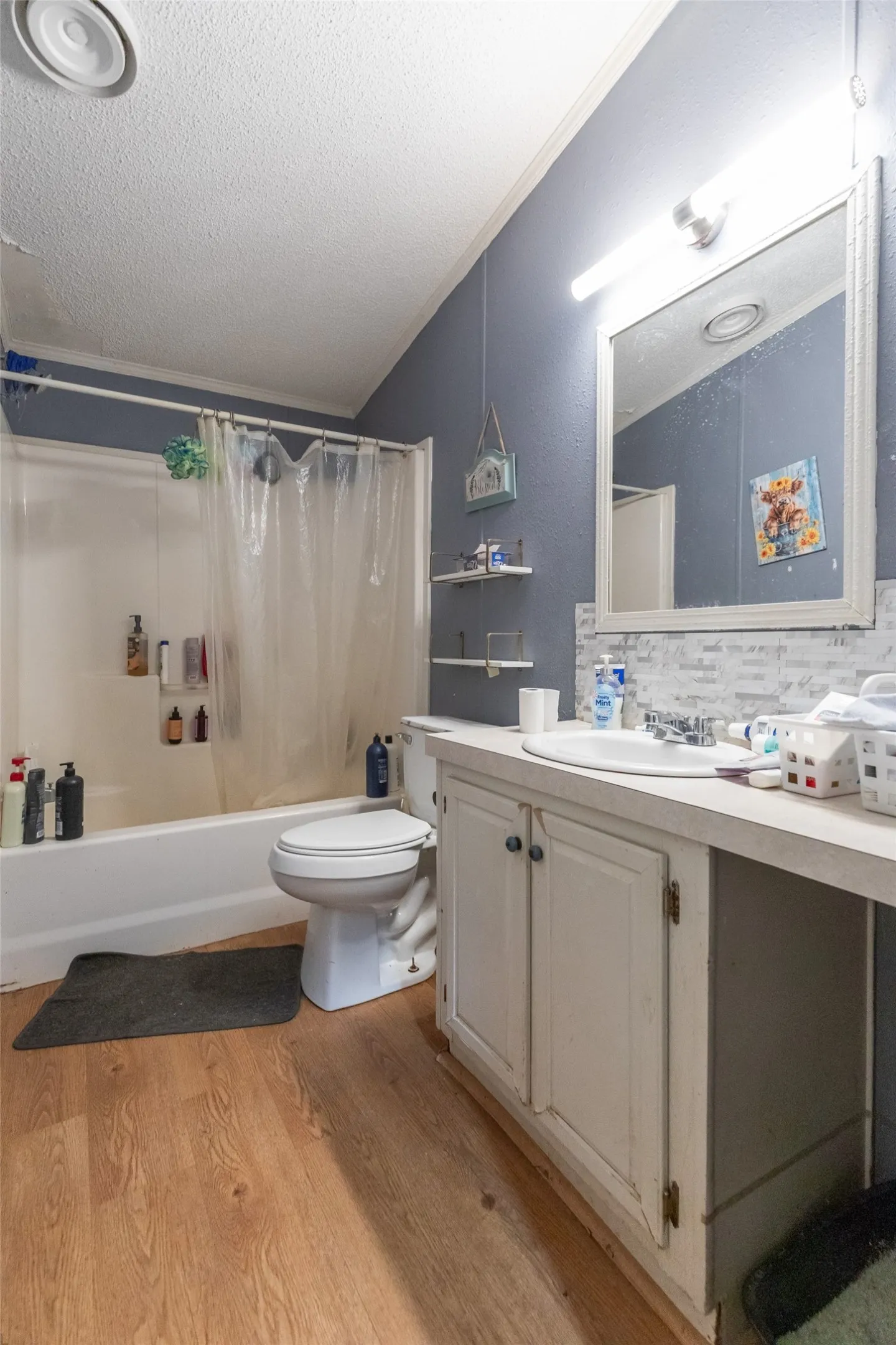 Bathroom featuring a full tub and shower combination, wood-finish flooring, a single vanity with storage, a large wall-mounted mirror, and a ceiling-mounted ventilation fan