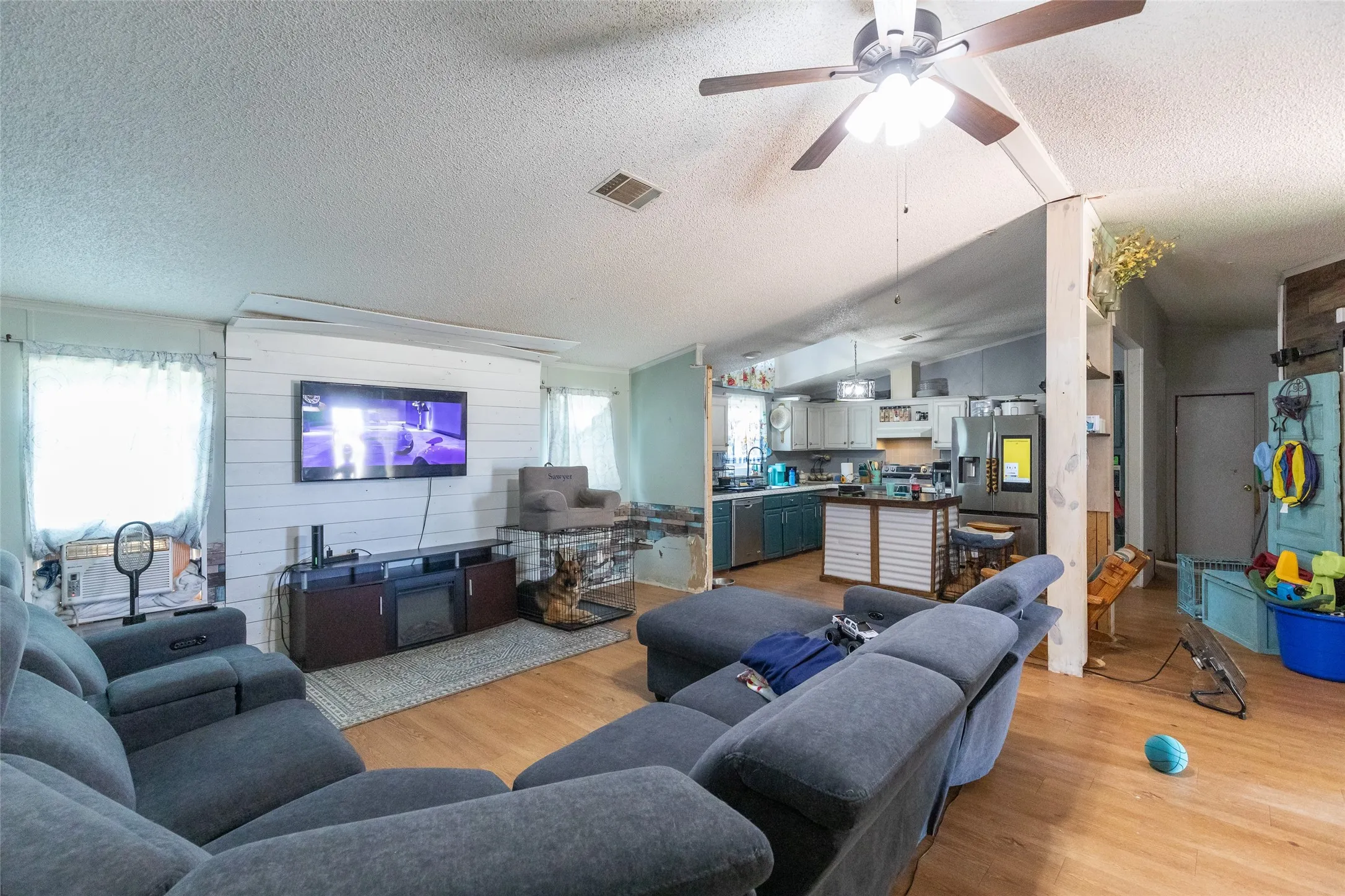 Spacious living area featuring wood-finish flooring, a ceiling fan, and shiplap wall accents